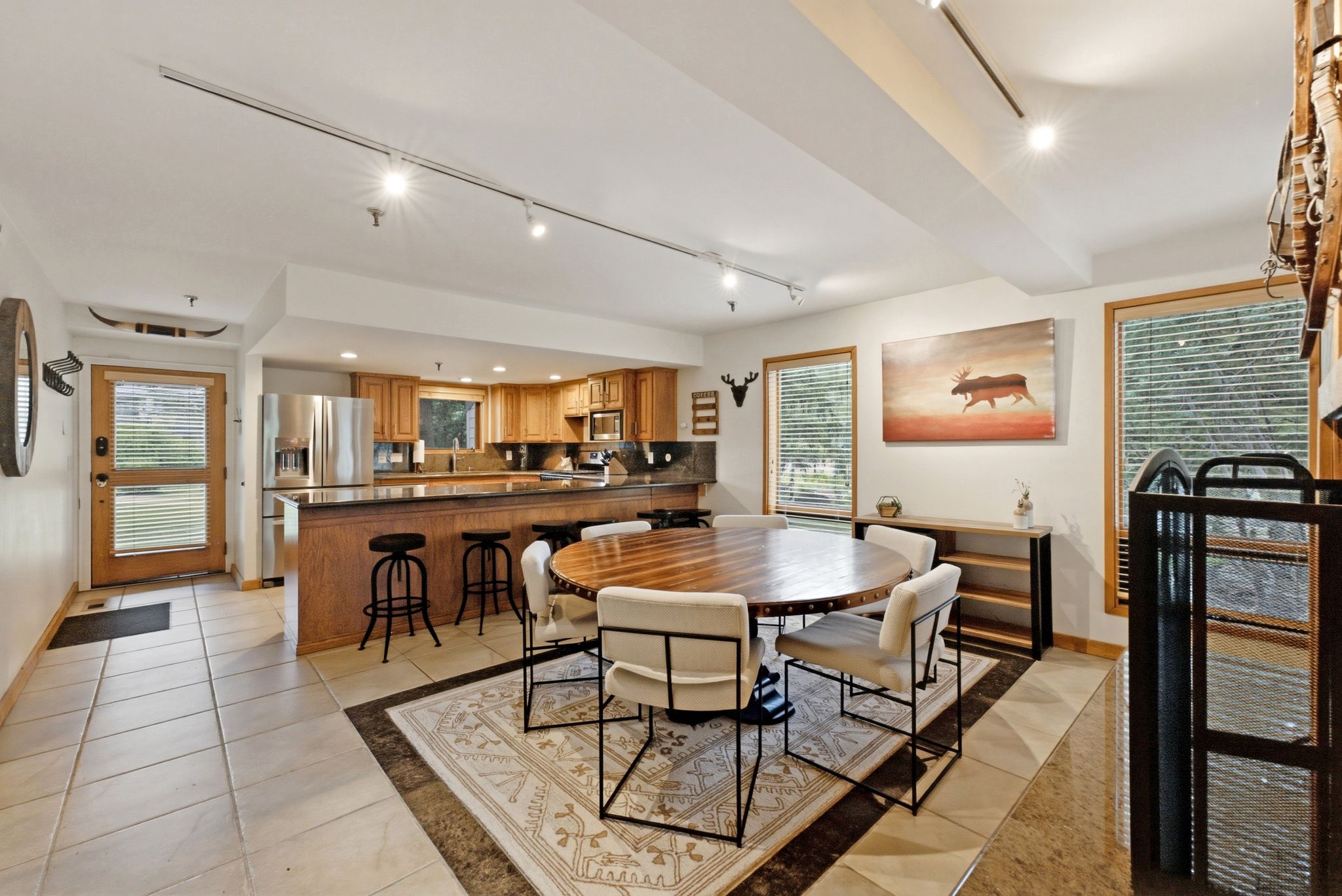 Open-concept living area featuring a kitchen with wood cabinetry and stainless steel appliances, a breakfast bar, and track lighting