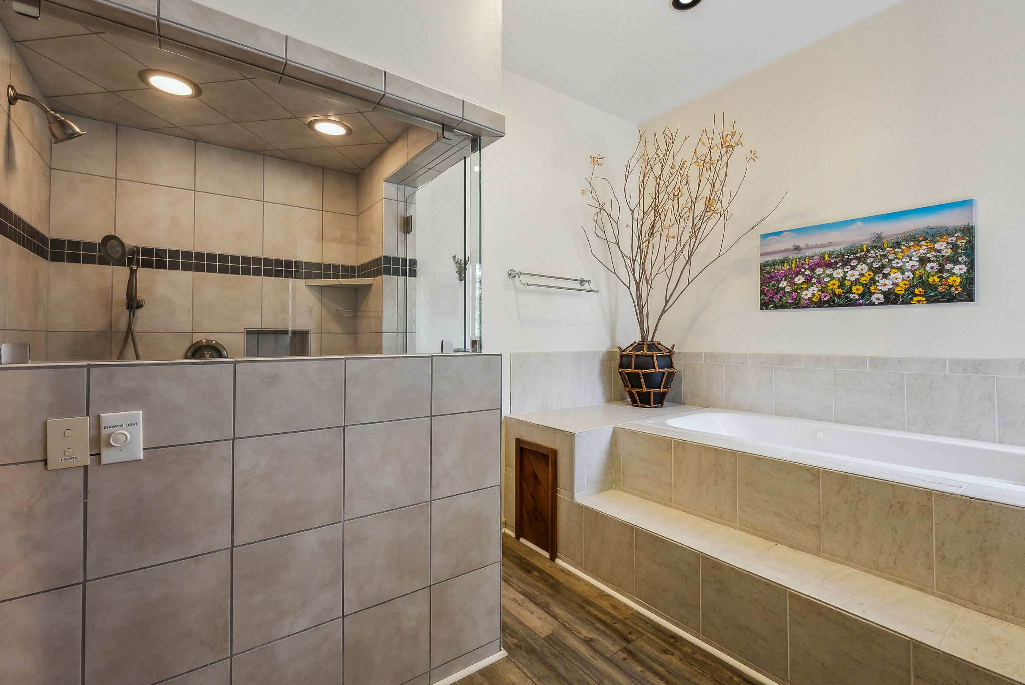 Spacious bathroom featuring a large walk-in shower with tile surround and glass enclosure, a built-in jetted tub with tile decking, recessed lighting, and wood-finish flooring