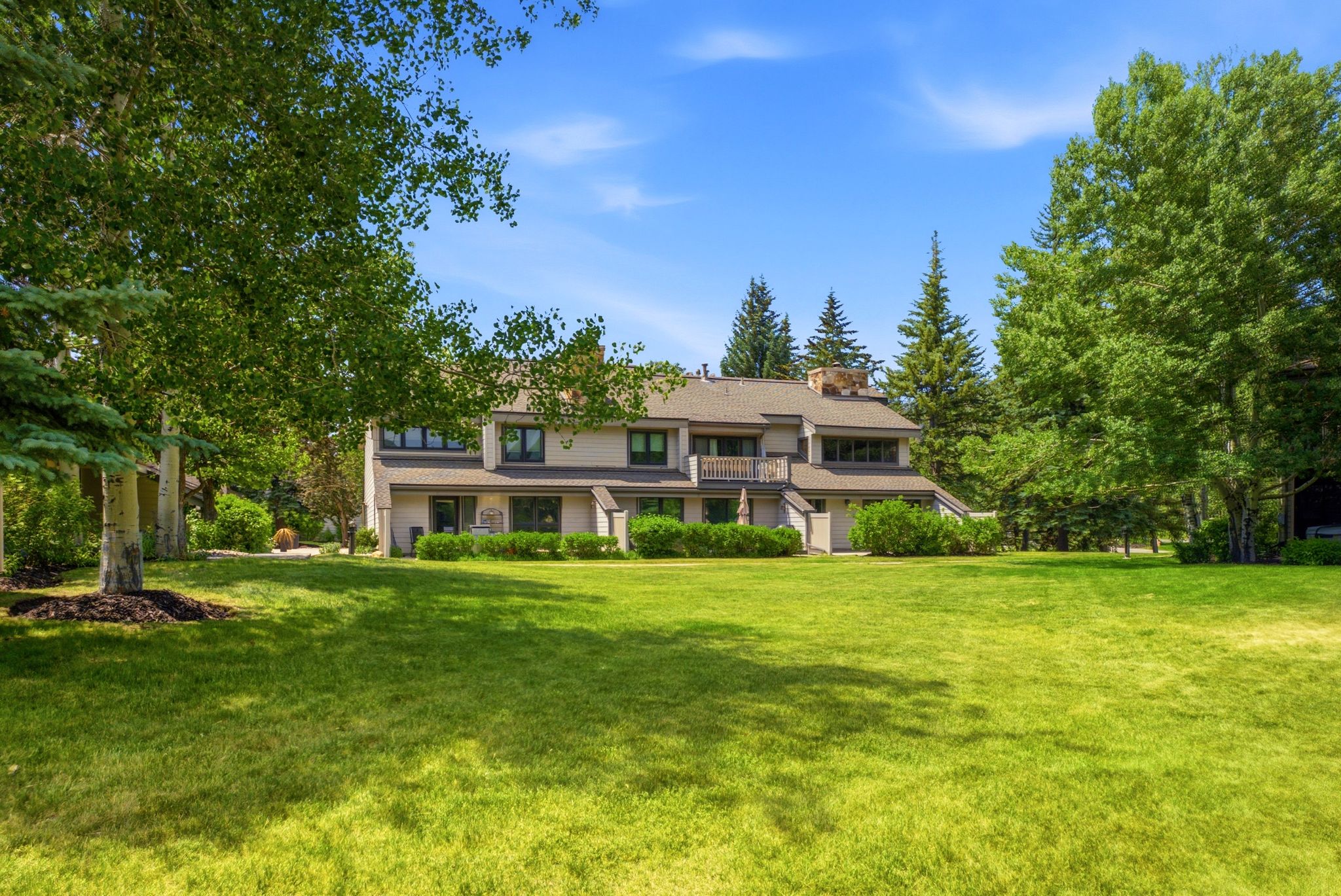 Expansive green lawn fronting a multi-level residence with a neutral-toned exterior, dark-framed windows, and an upper-level balcony