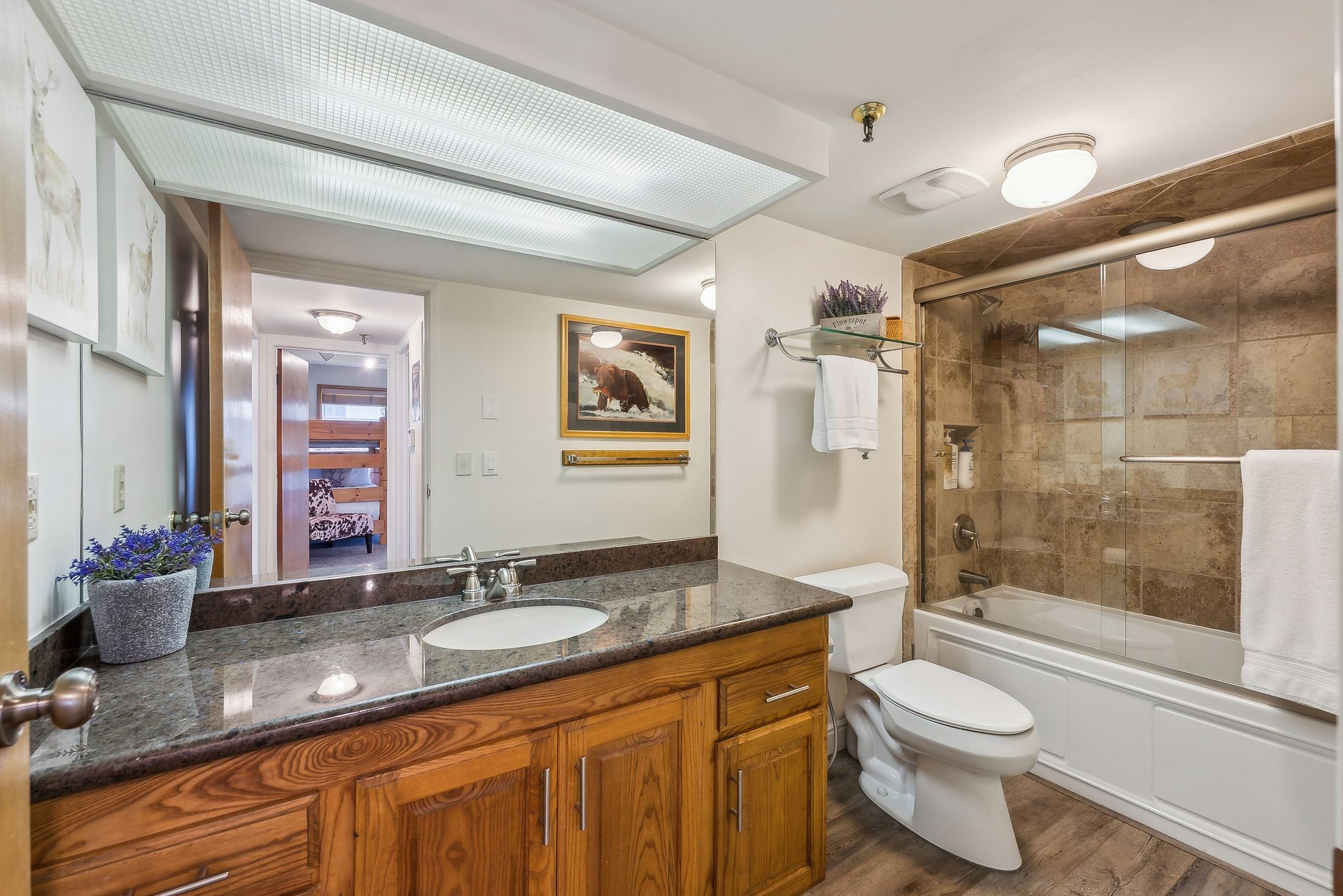 Bathroom featuring a wood vanity with a granite-style countertop, a drop-in sink, and a large wall mirror