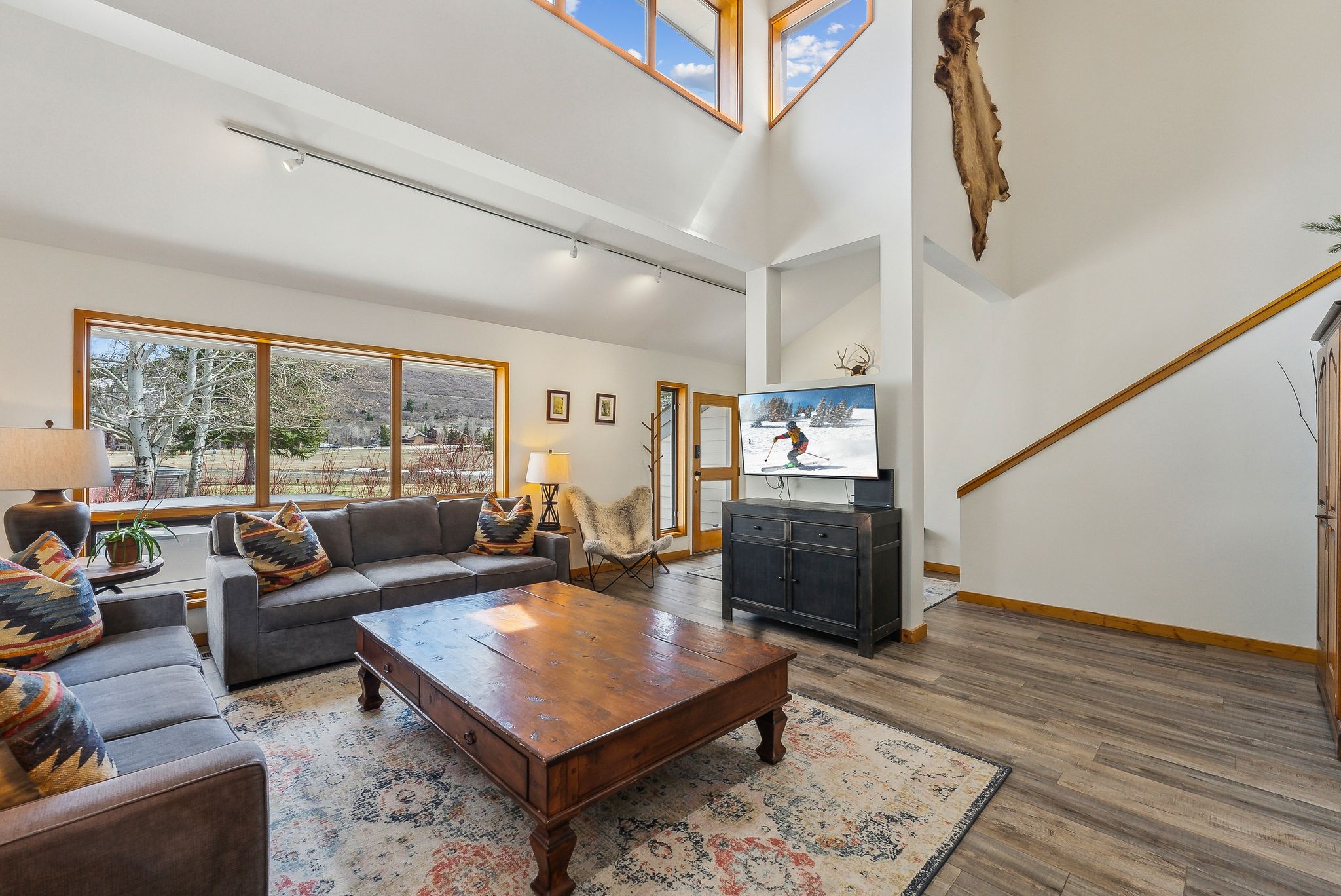 Vaulted ceilings with upper-level windows, large picture windows, wood-finish flooring, a multi-pane glass door, and track lighting