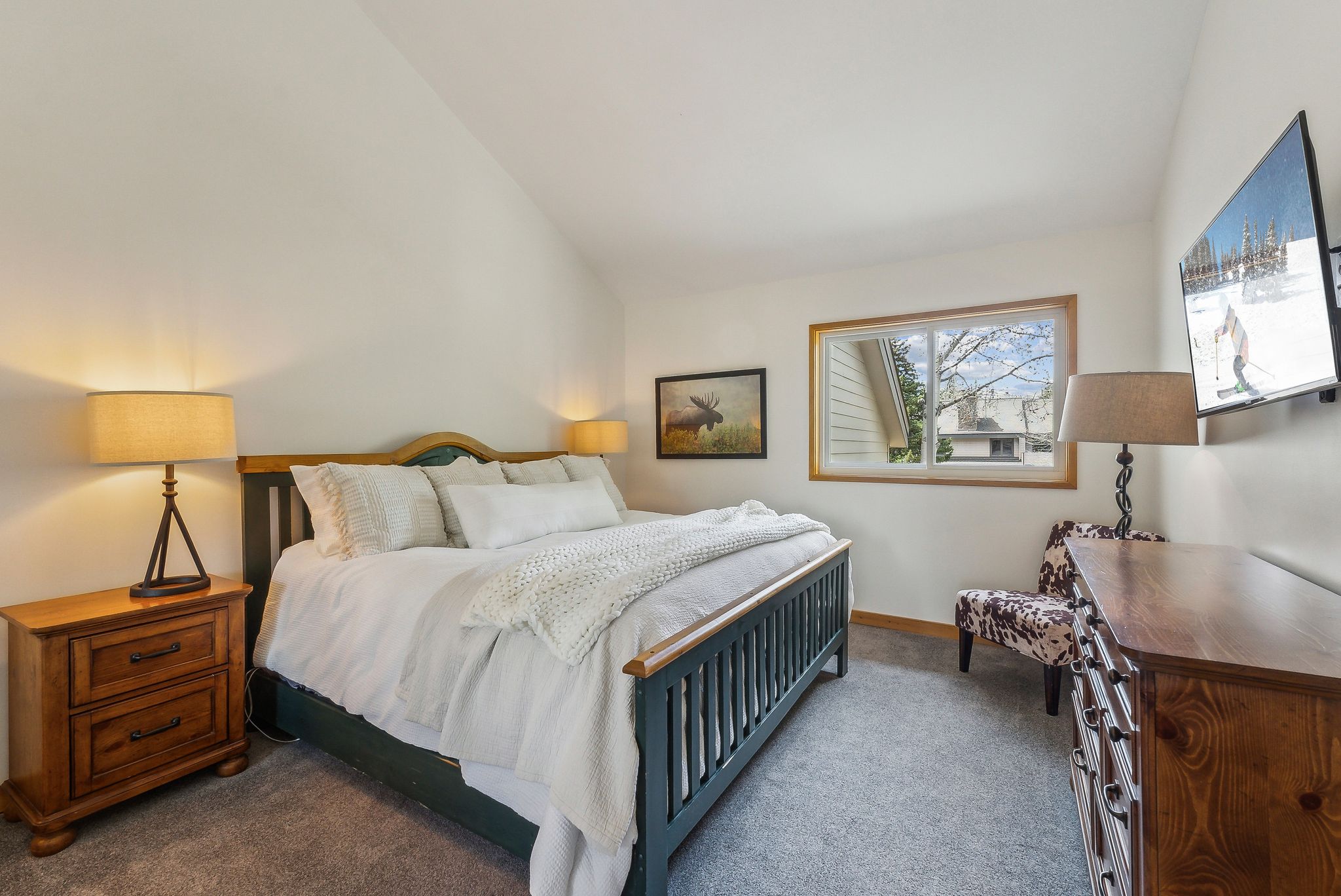 Vaulted ceilings crown this bedroom space, featuring light-toned carpeting and a window with wood trim