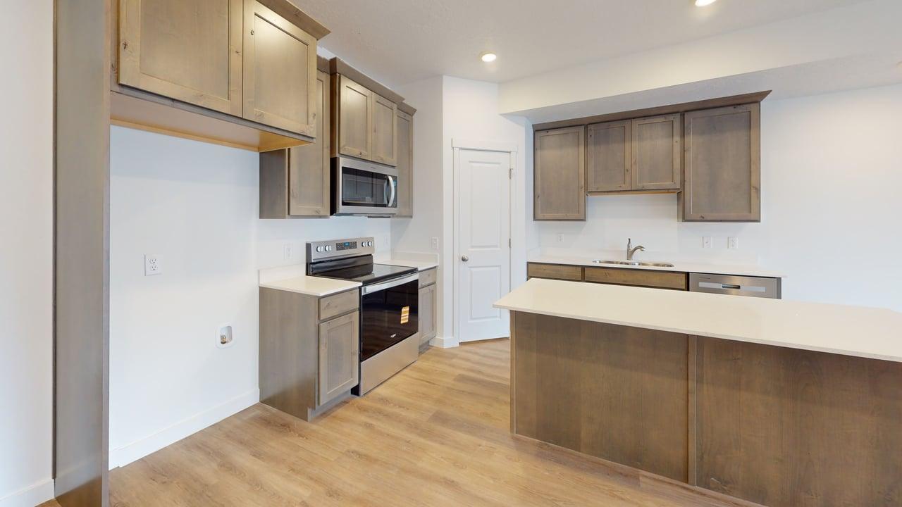 Contemporary kitchen featuring wood-finish flooring, light wood-tone cabinetry, stainless steel appliances, a white subway tile backsplash, and an island with a light-toned countertop