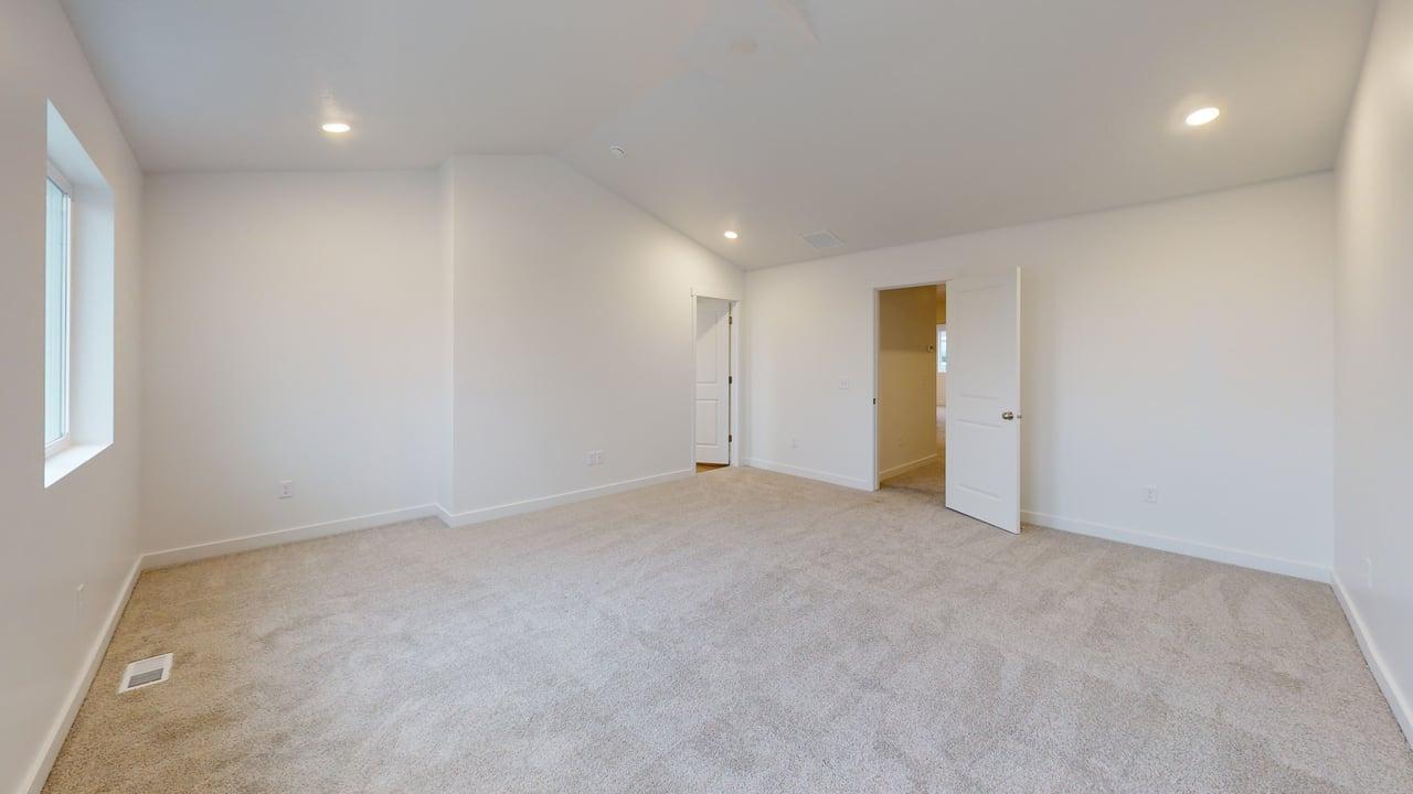 Spacious room featuring light-toned carpeting, white walls, recessed lighting, and a window providing natural light