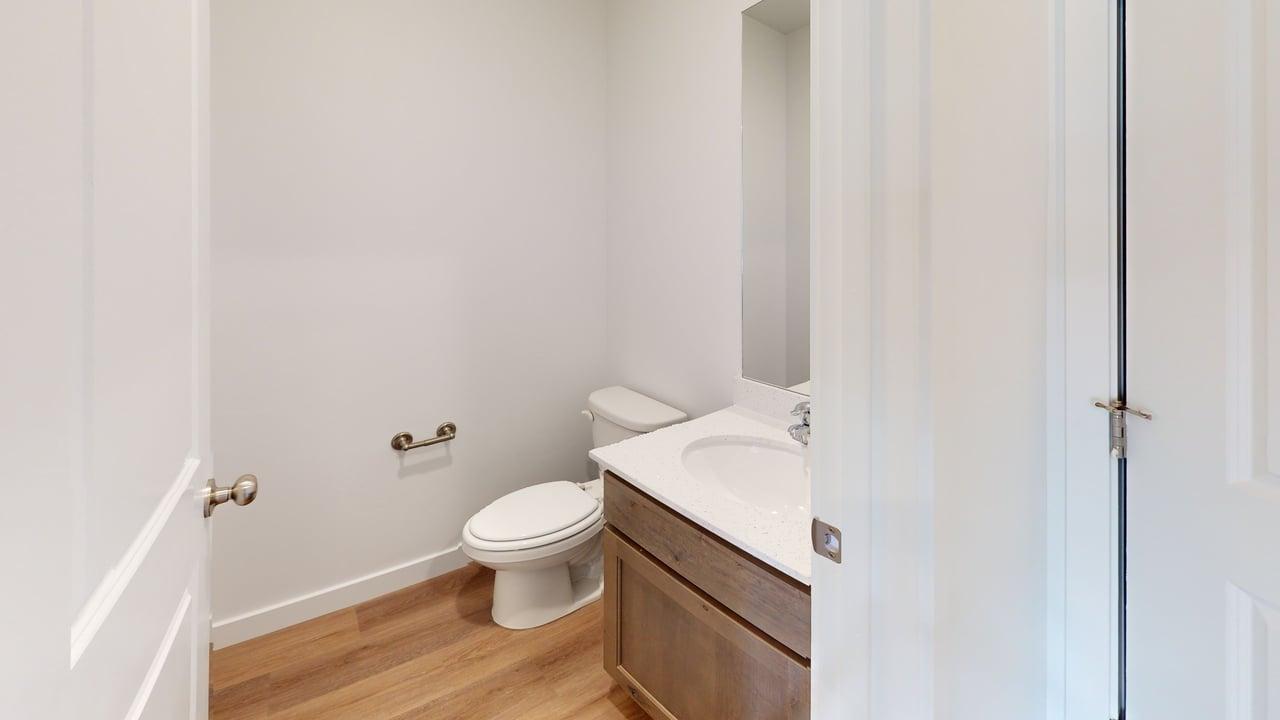 Powder room featuring light wood-finish flooring, a white vanity with an integrated sink, a wall-mounted mirror, and a modern toilet