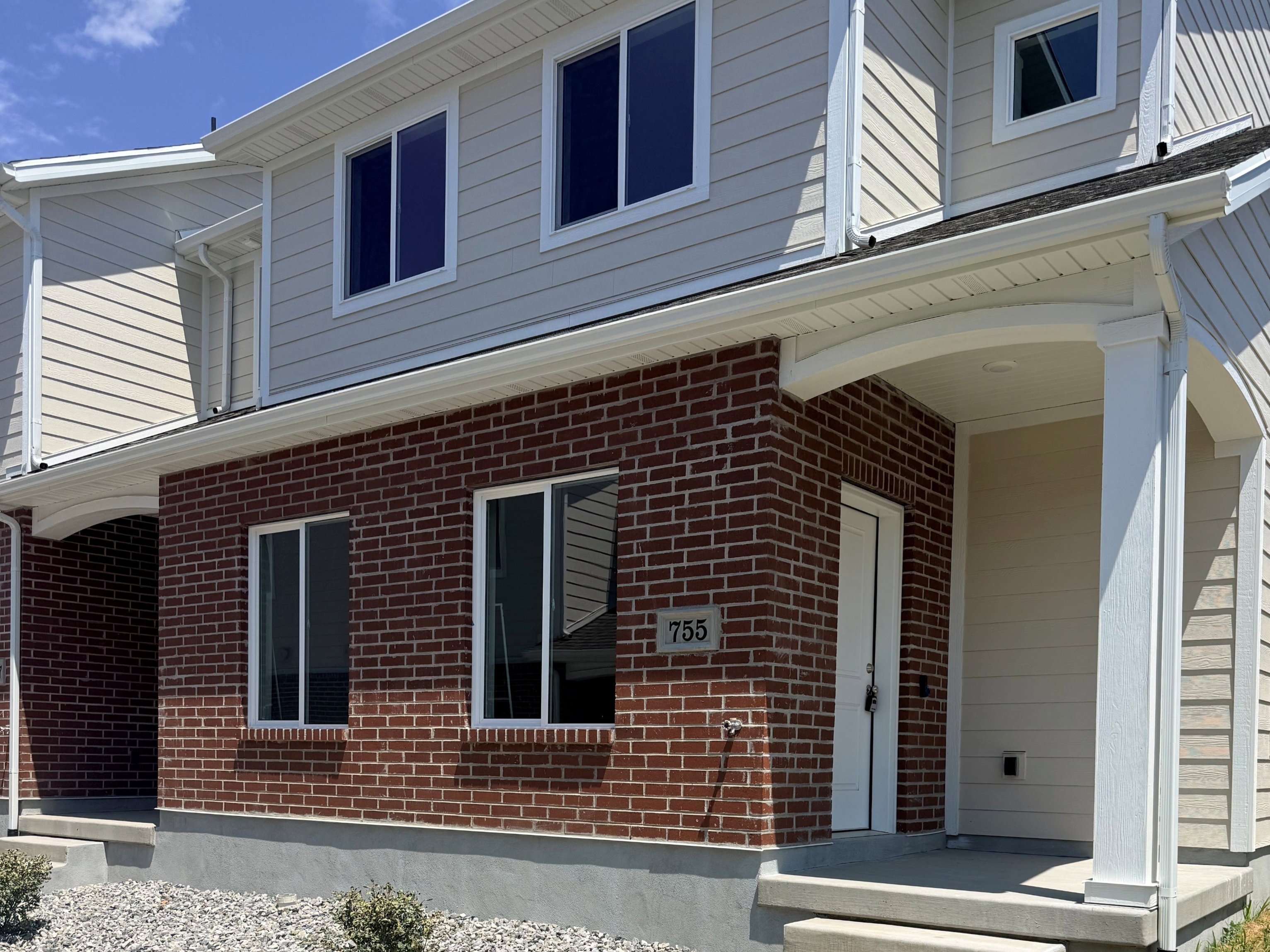 Two-story brick and siding construction featuring a covered front entry with white columns and a concrete walkway