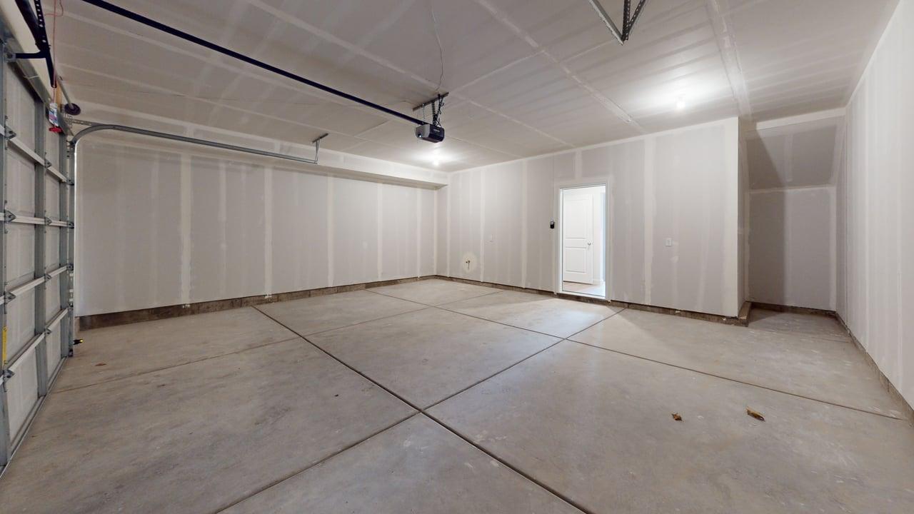 Spacious garage featuring a concrete floor, high ceilings, exposed drywall, and a white interior door