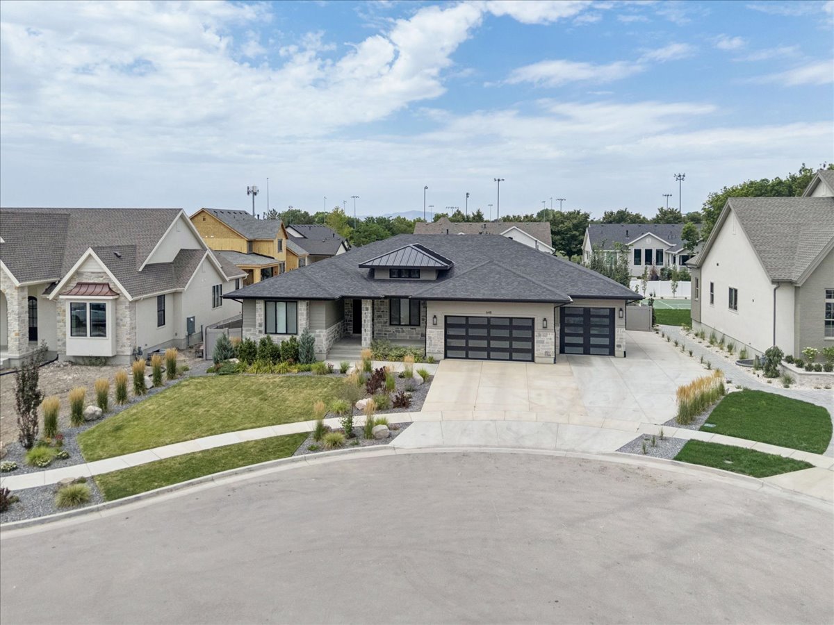 Contemporary single-story residence featuring a dark gray roof, stucco and stone exterior, two modern garage doors with frosted glass panels, an arched entry portico, and a concrete driveway