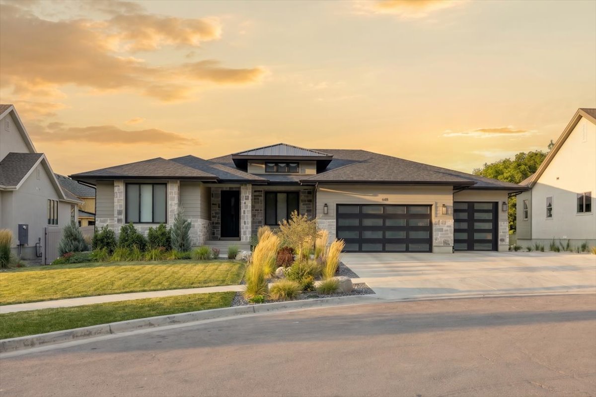 Modern residence featuring a stone and stucco exterior, prominent dark-framed windows, and a multi-car garage with contemporary glass panel doors