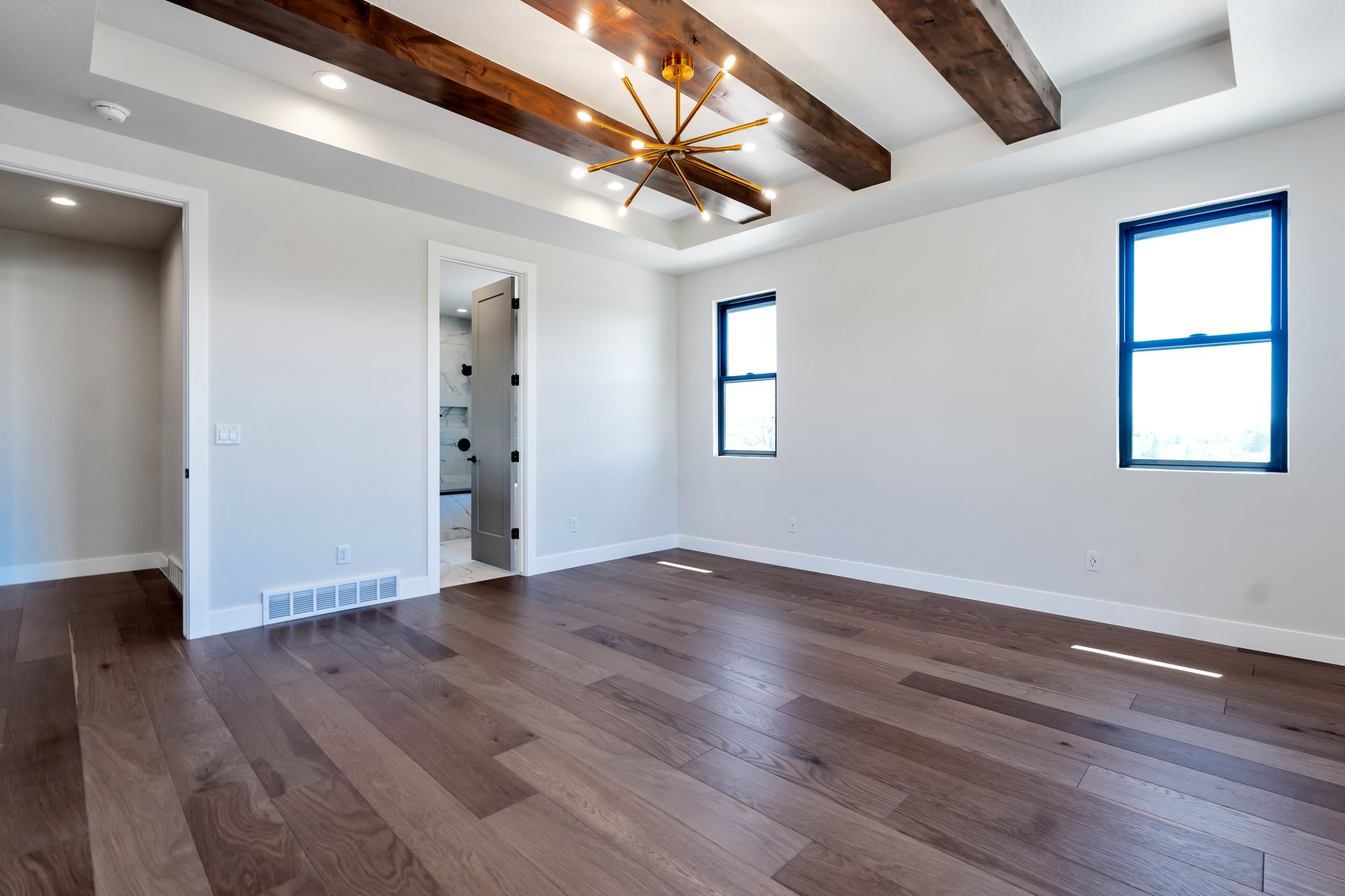 Spacious room featuring wood-finish flooring, a coffered ceiling with exposed wood beams, and a modern chandelier