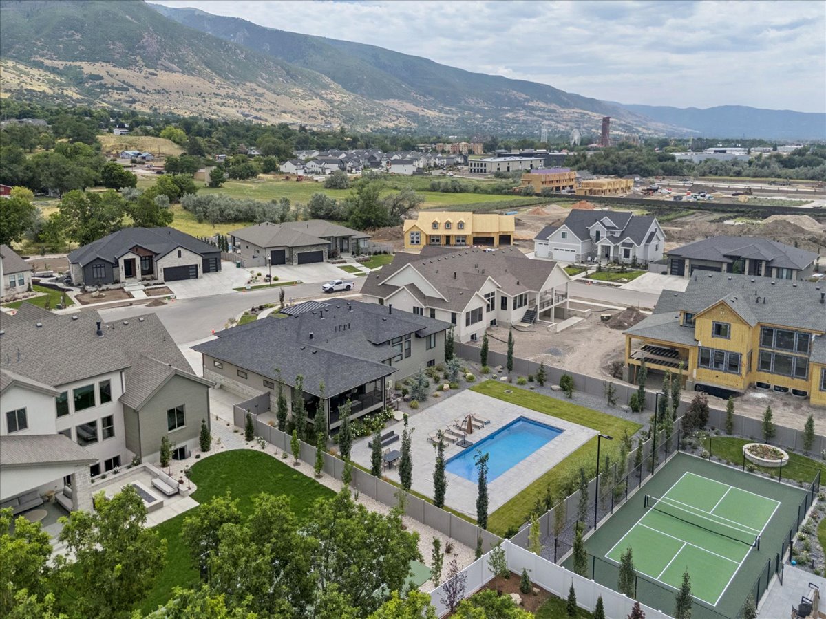 Private tennis court with surrounding fencing, adjacent swimming pool, manicured lawn, and mature landscaping