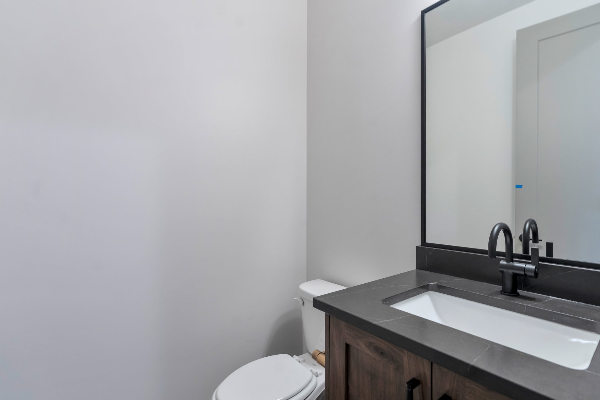 Bathroom vanity featuring a dark wood-finish cabinet with black hardware, a dark countertop with an integrated white rectangular sink, and a matte black faucet