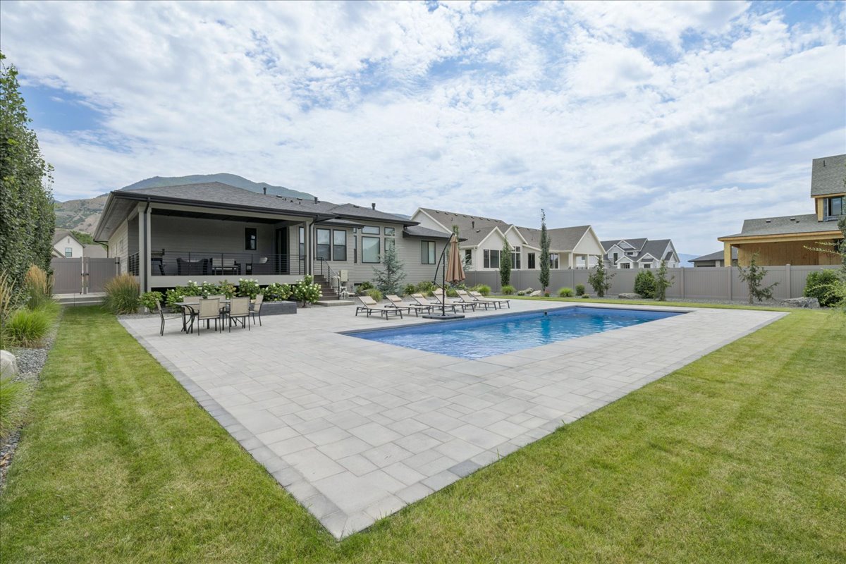 Expansive backyard featuring a rectangular swimming pool, large paver patio, and a covered patio area with a dark railing