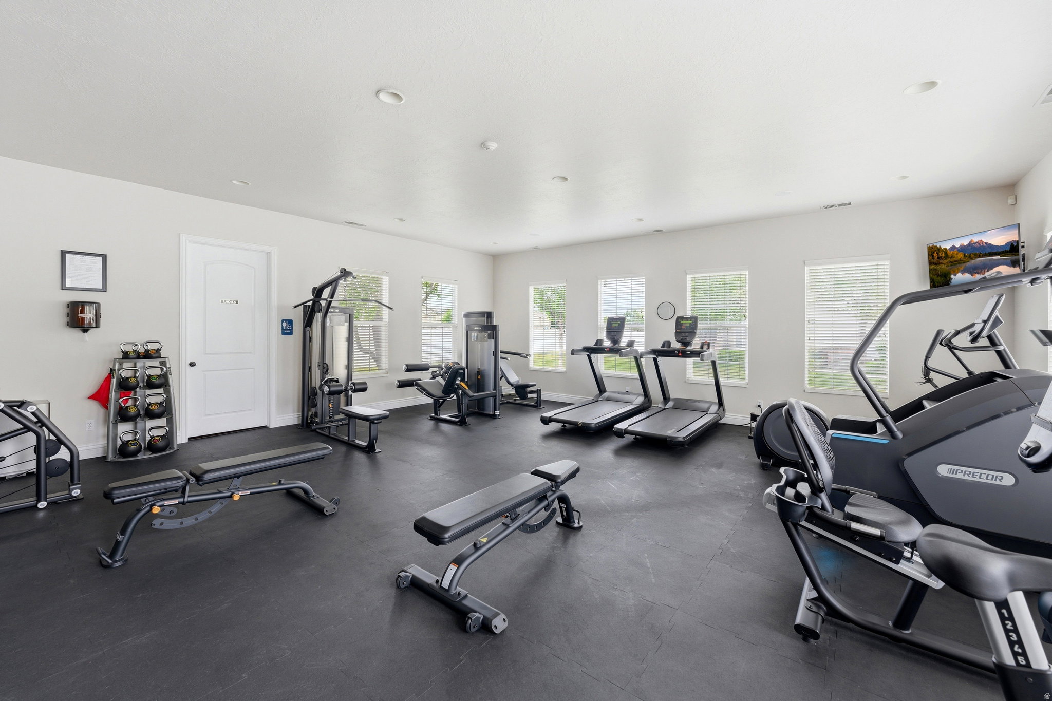 Dedicated exercise room featuring dark rubber flooring, white walls, recessed lighting, and multiple windows