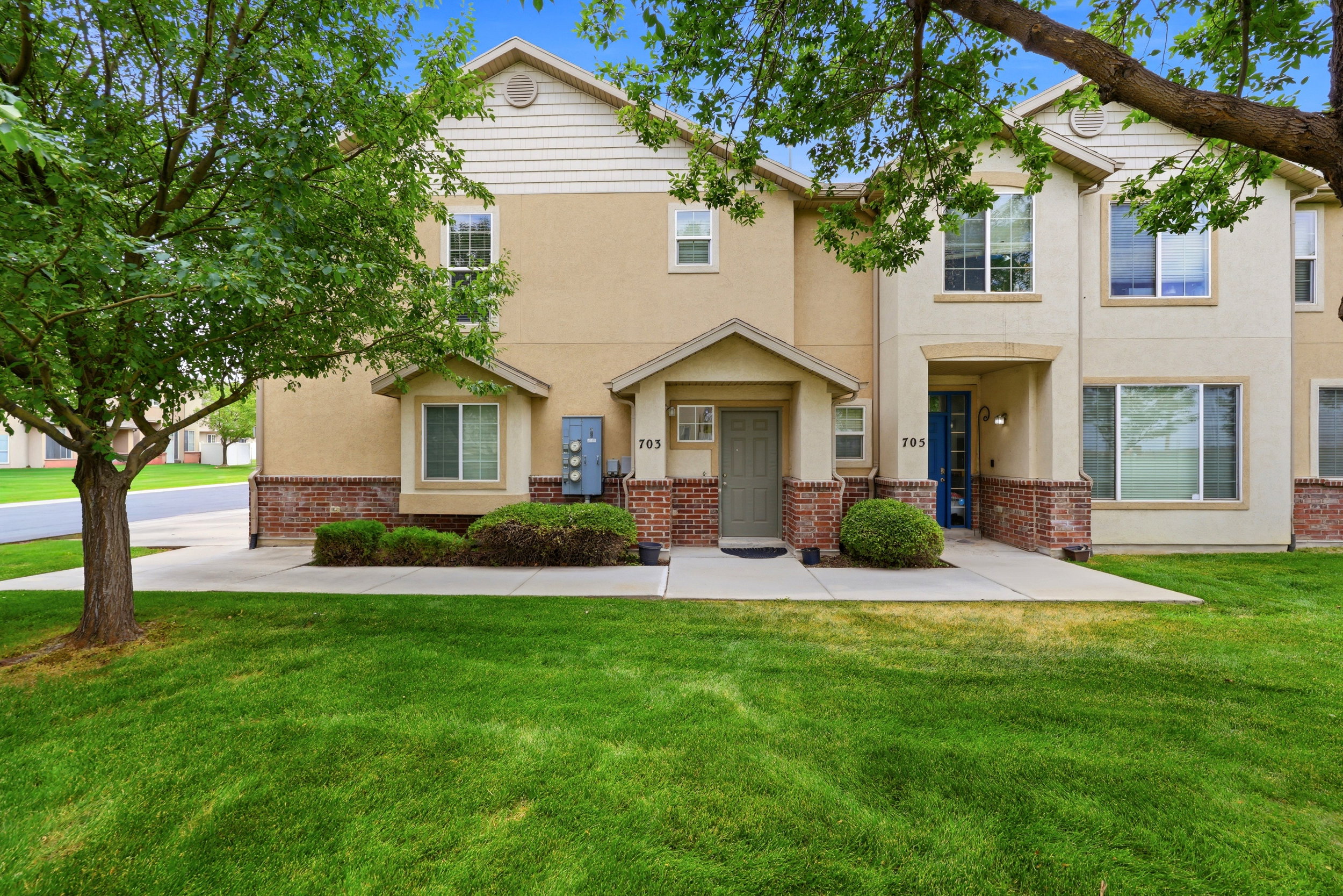 Townhome exterior featuring tan stucco siding with brick veneer accents, a covered entry, and individual front doors