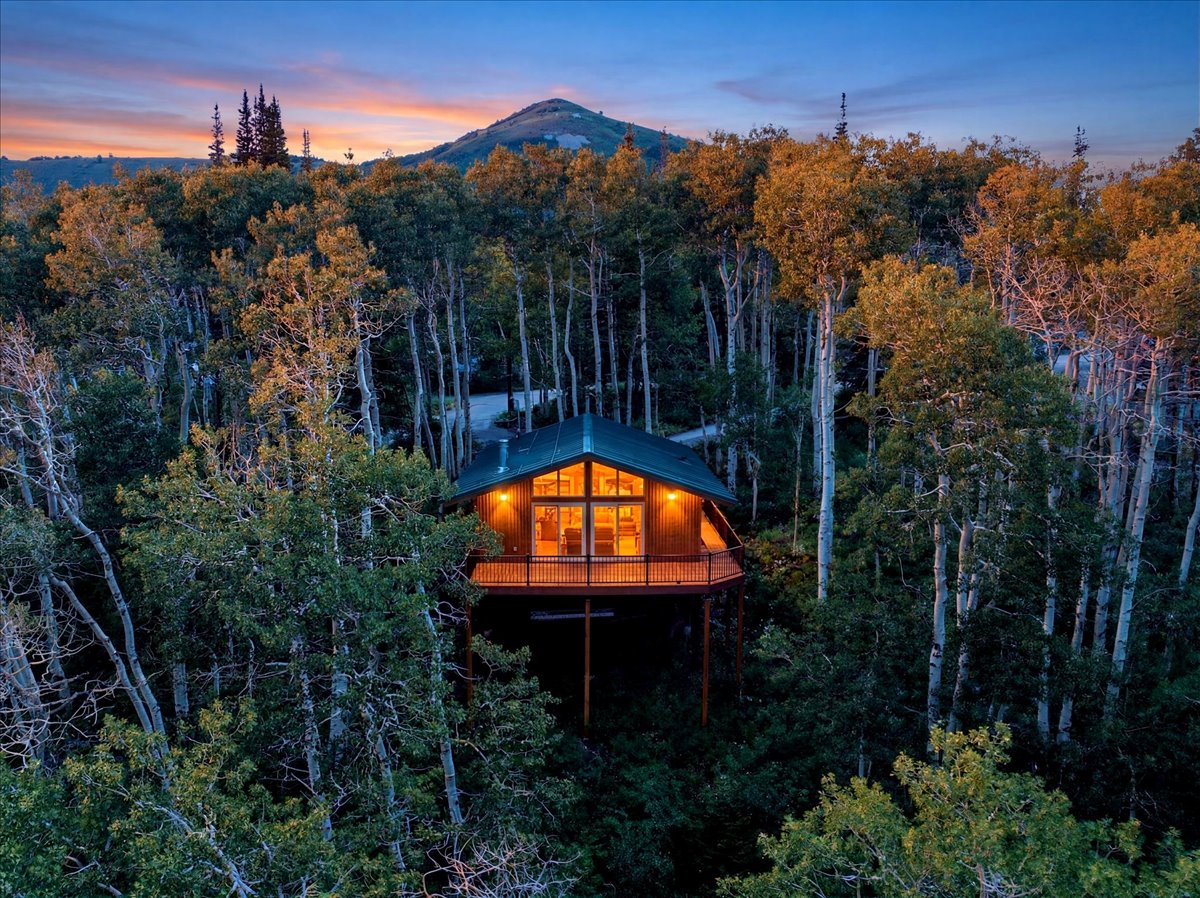 Elevated wood-sided residence featuring a dark-pitched roof, expansive windows, and an outdoor deck