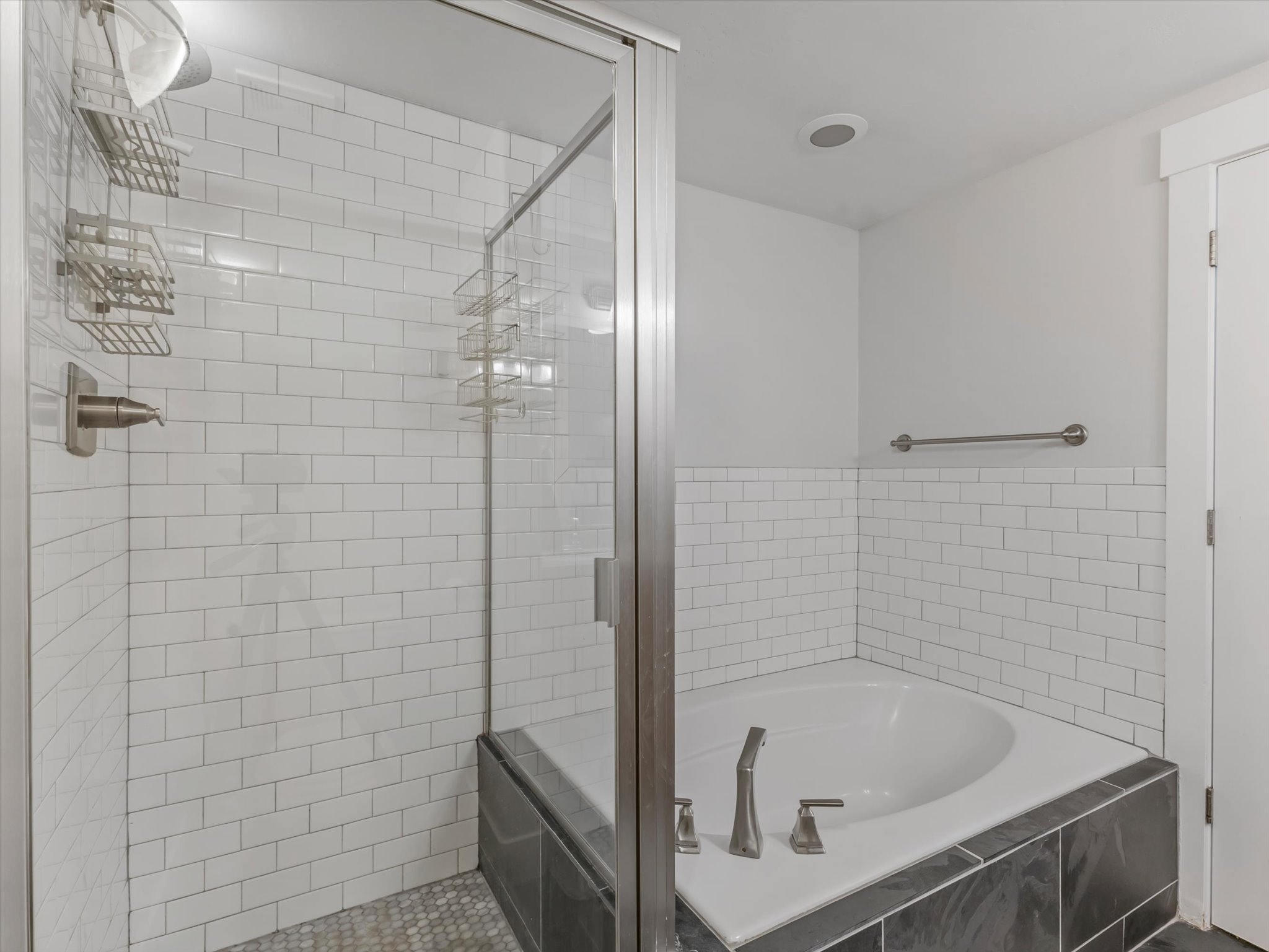 Bathroom featuring a subway tile shower enclosure with a glass door, a dark tile shower pan, and a built-in corner soaking tub with dark tile surround