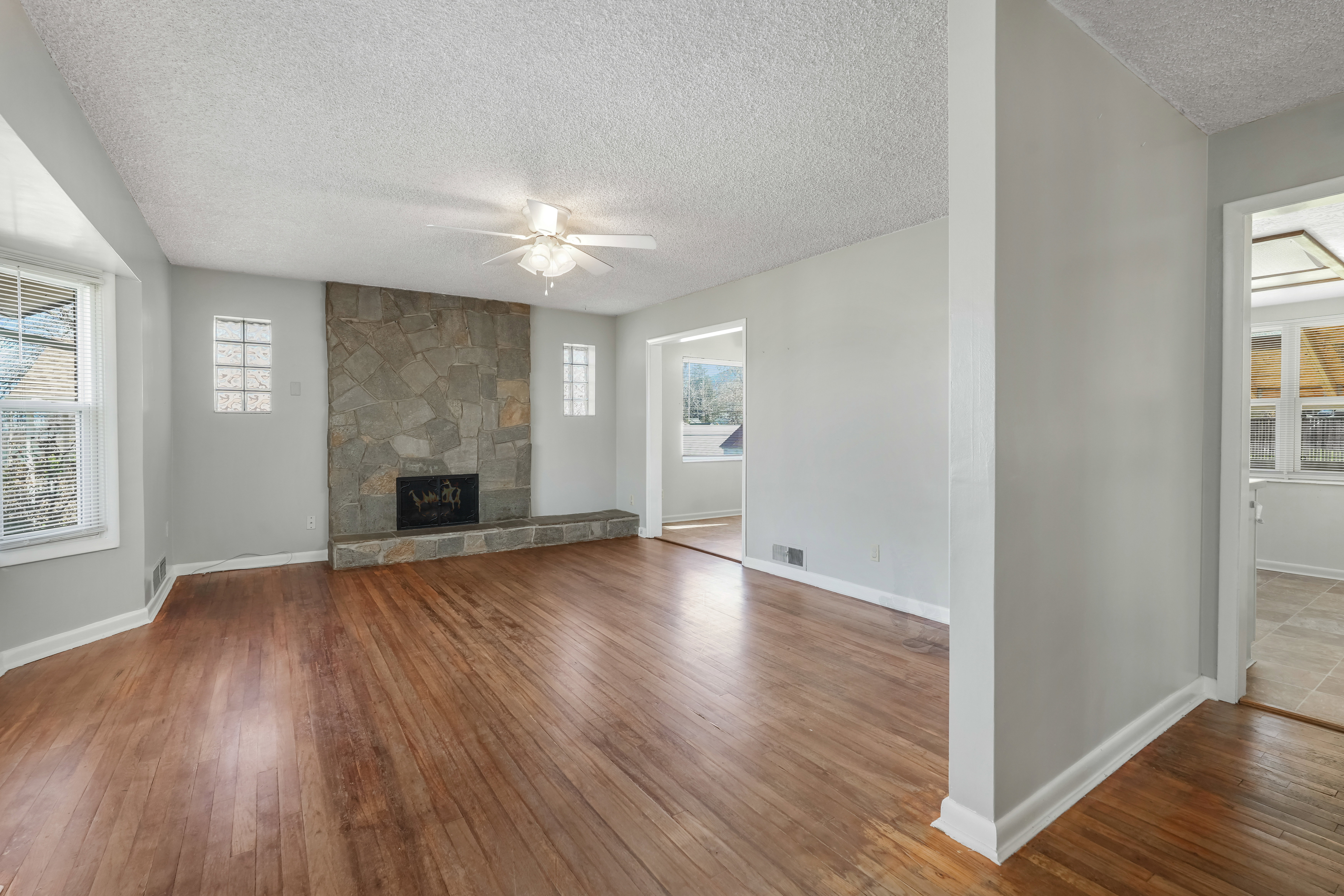 Spacious living area featuring wood-finish flooring, a stone-clad fireplace, and multiple windows