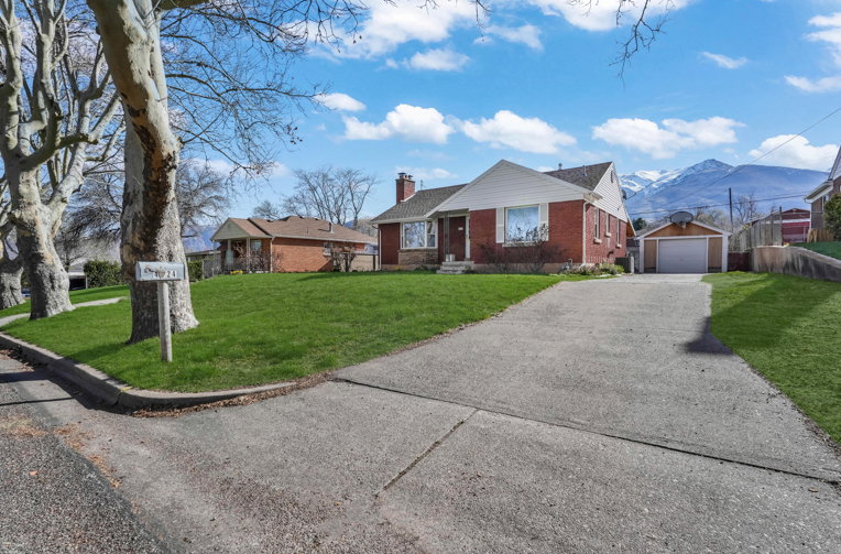 Brick home with a pitched roof, front lawn, paved driveway, detached garage, and mountain backdrop