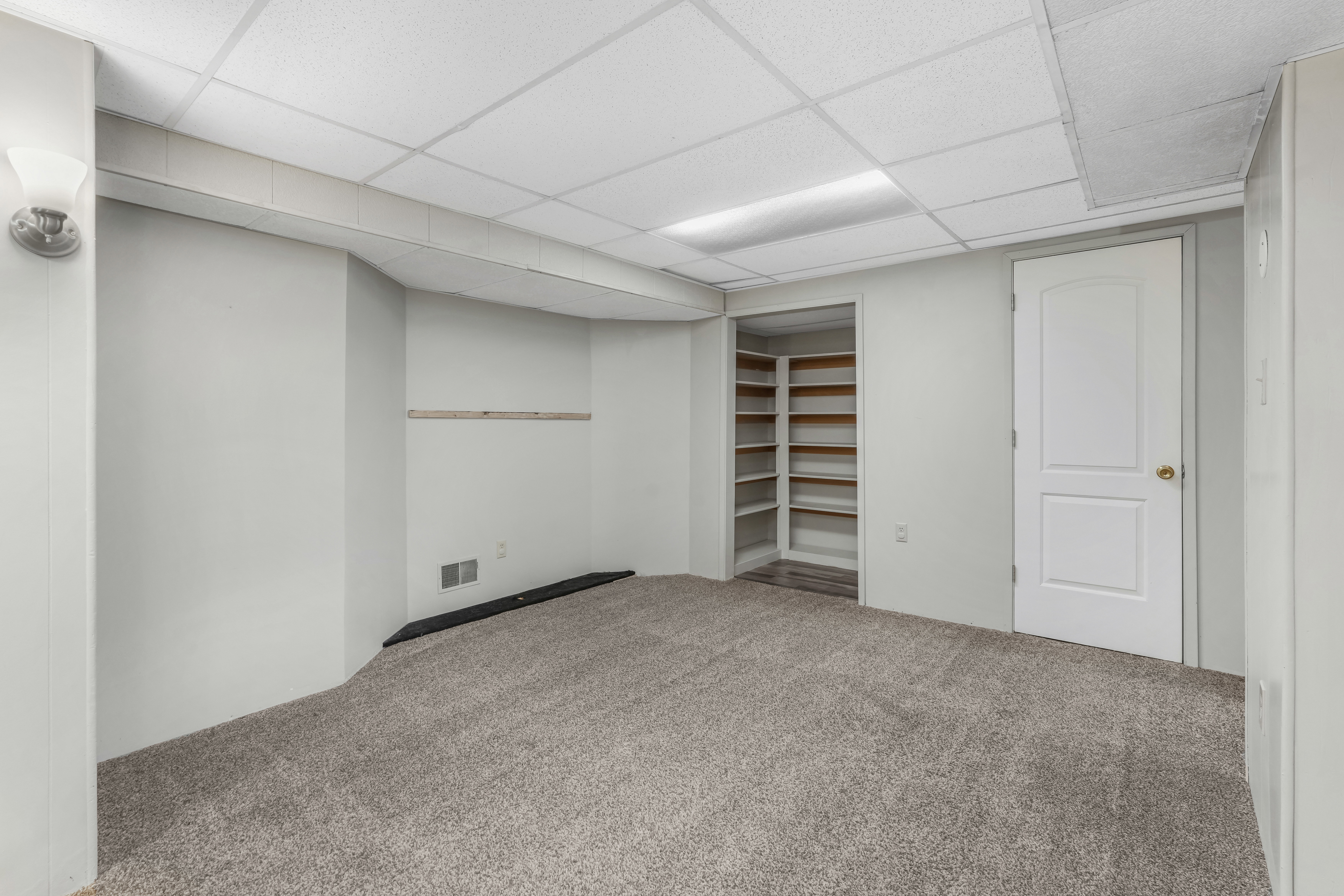 Carpeted interior space featuring light gray walls, a drop ceiling, and a built-in shelving unit