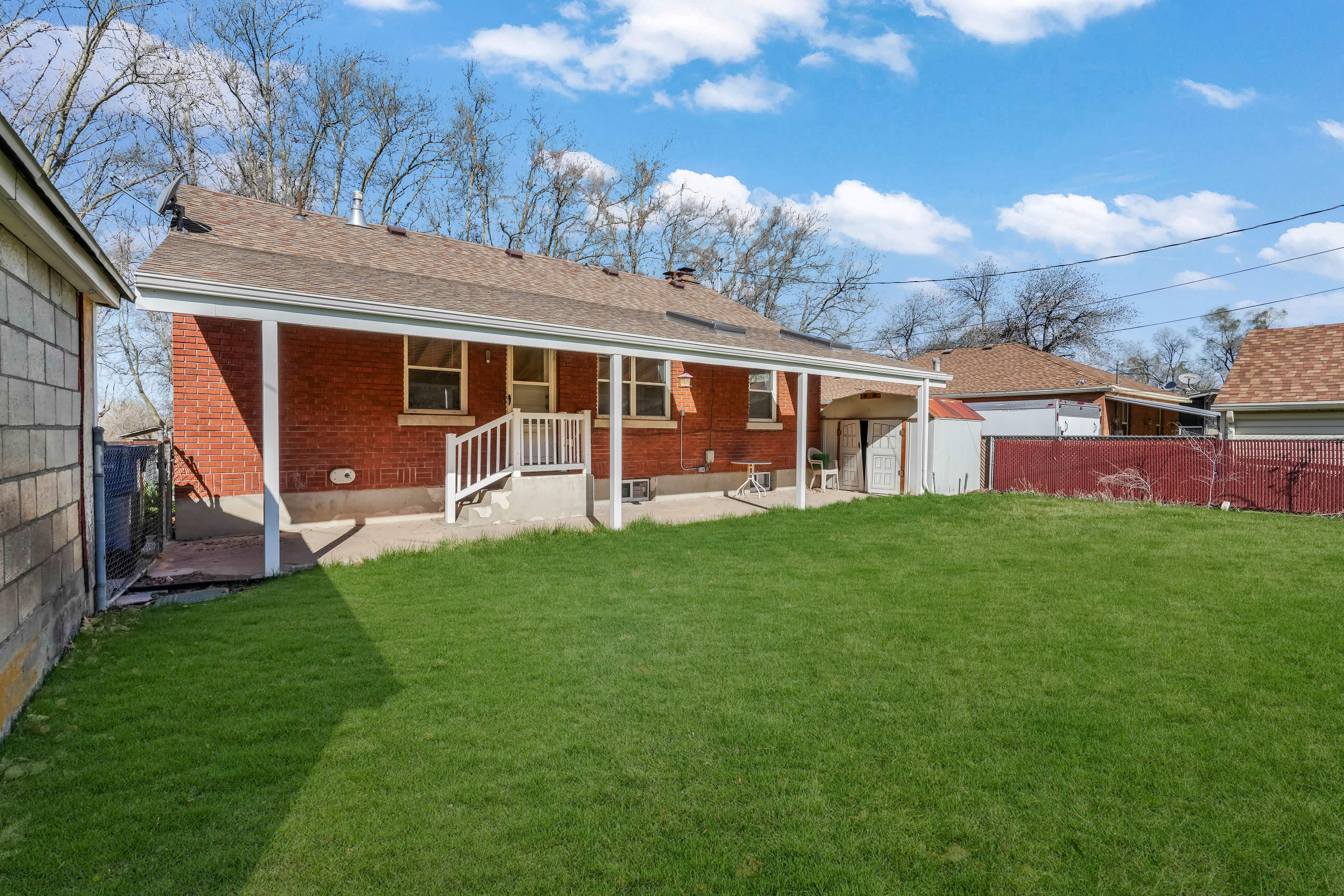 Expansive green lawn with a covered concrete patio, brick exterior, and white railing leading to the back entrance