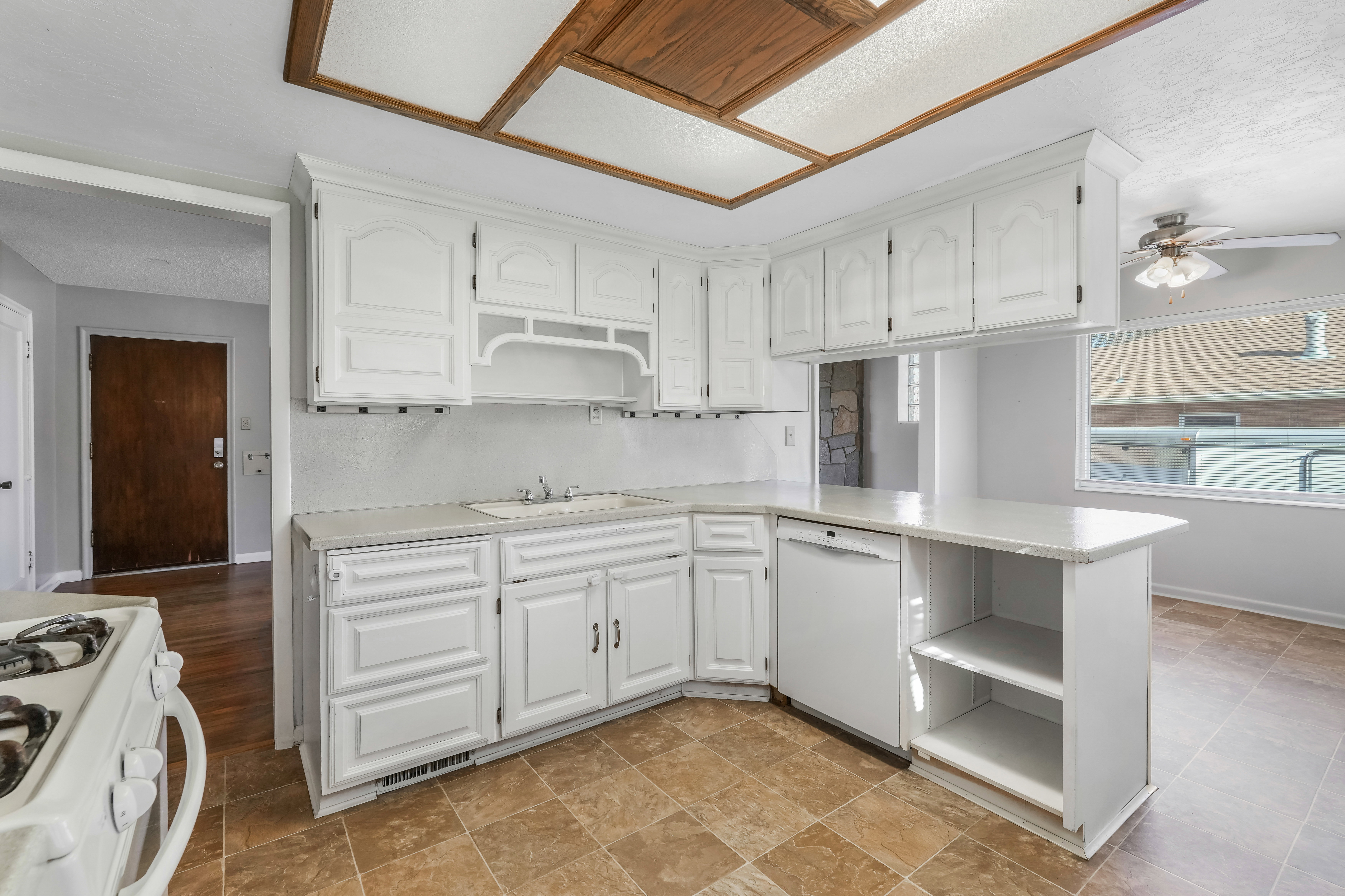 Kitchen featuring white cabinetry, a built-in dishwasher, and a breakfast bar with open shelving
