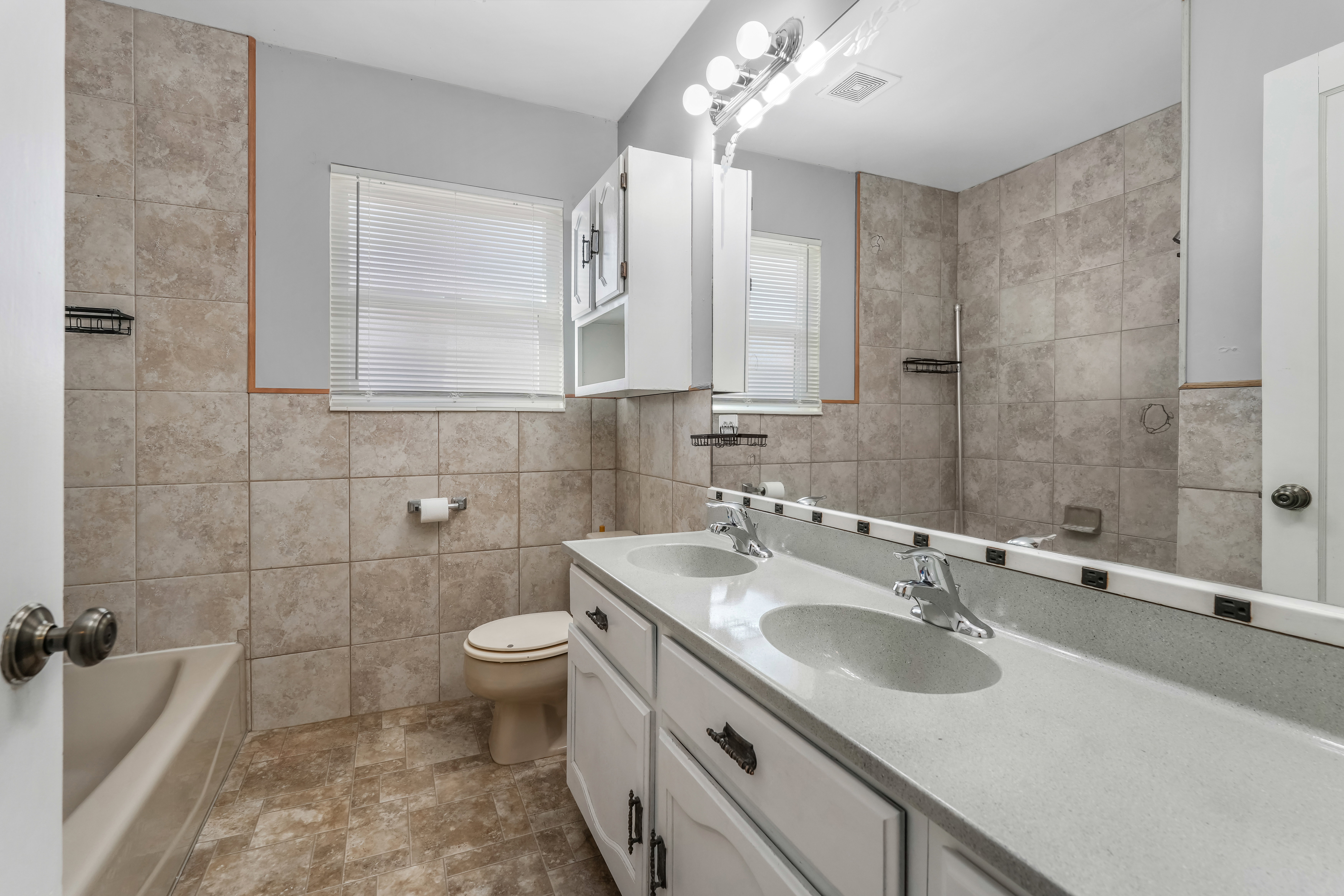 Bathroom featuring a dual-sink vanity with white cabinetry, a large mirror, and overhead vanity lighting