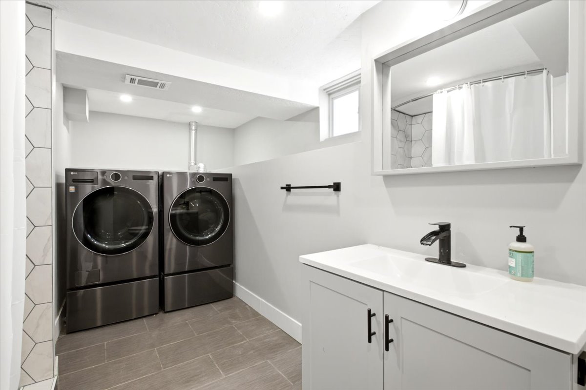 Spacious laundry and bathroom, updated with new vanity, fixtures, and floor to ceiling tile shower surround.