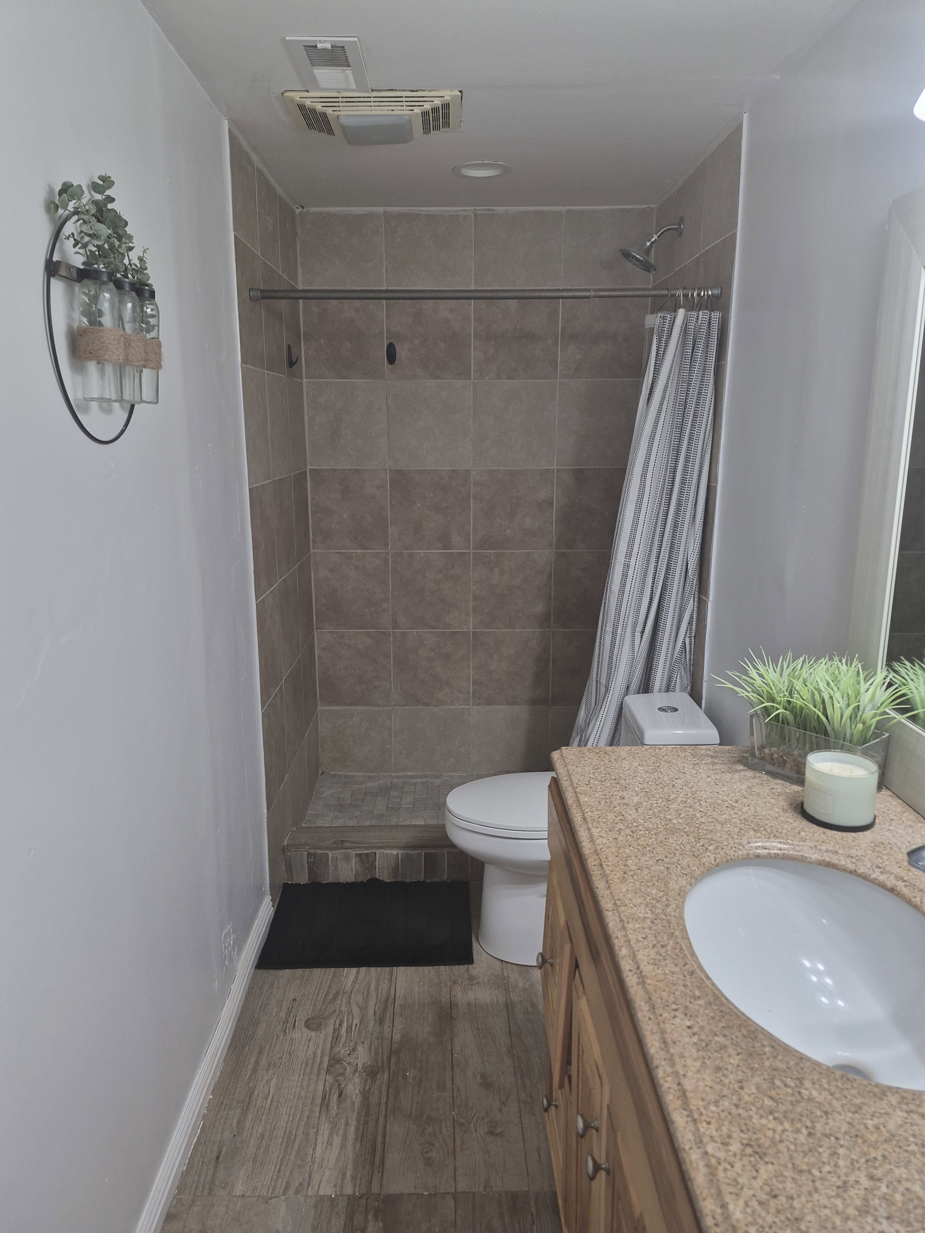 Bathroom featuring a tiled walk-in shower with showerhead, wood-finish flooring, a vanity with an integrated sink and light-colored countertop, and a toilet