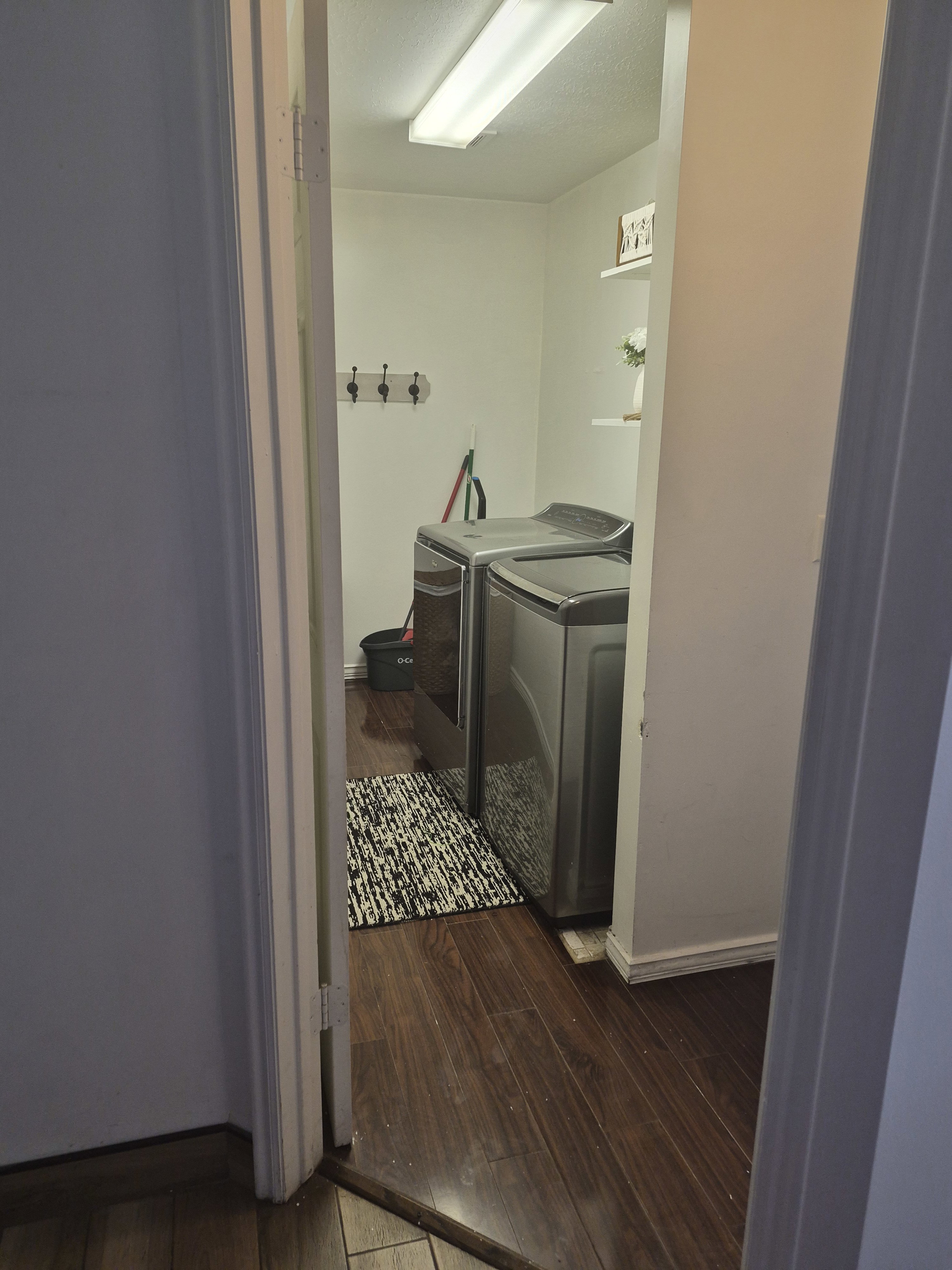 Laundry area featuring wood-finish flooring, white walls, built-in wall shelves, and a wall-mounted coat rack