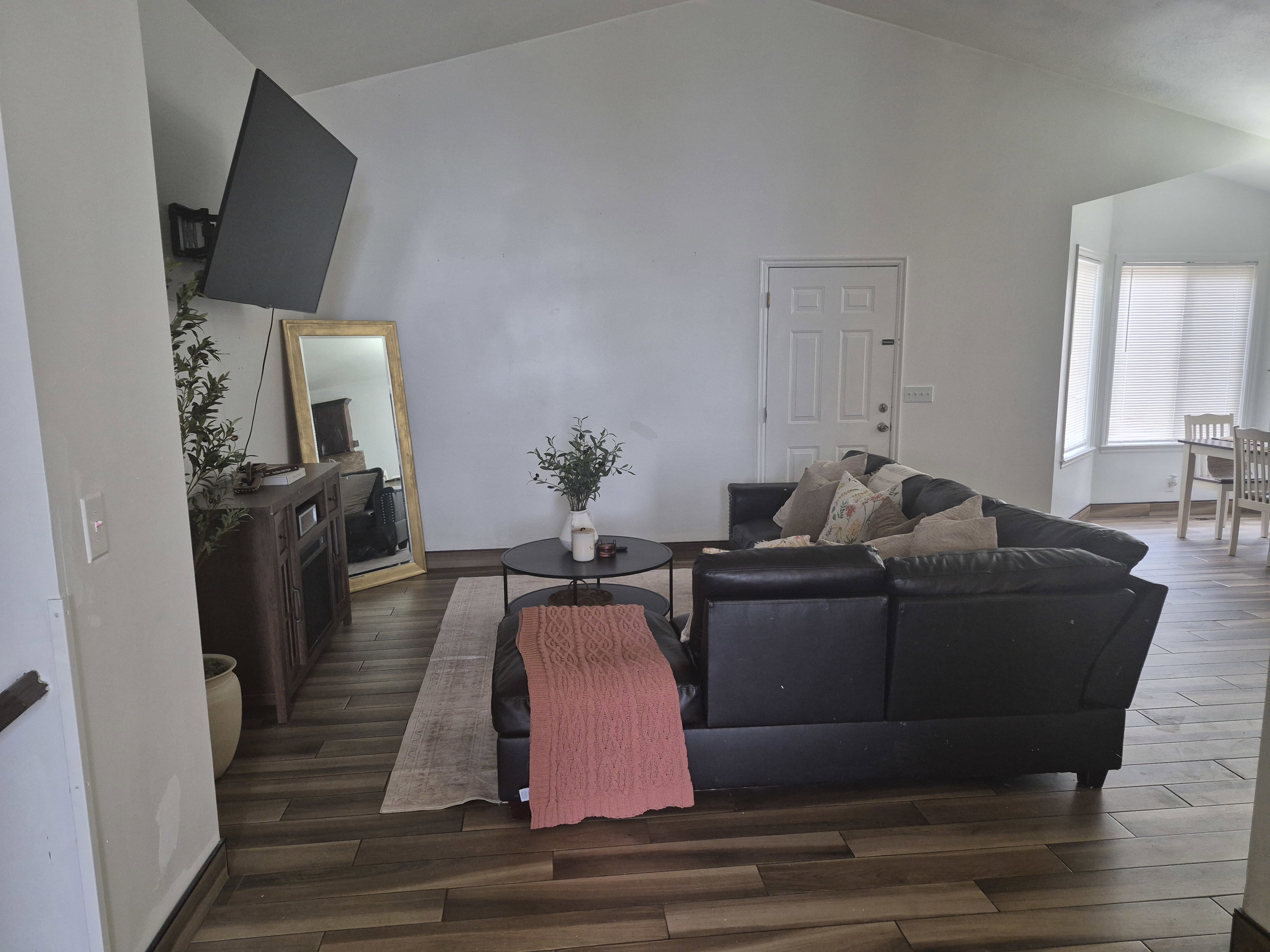 Spacious living area featuring vaulted ceilings, wood-finish flooring, a paneled entry door, and large bay windows