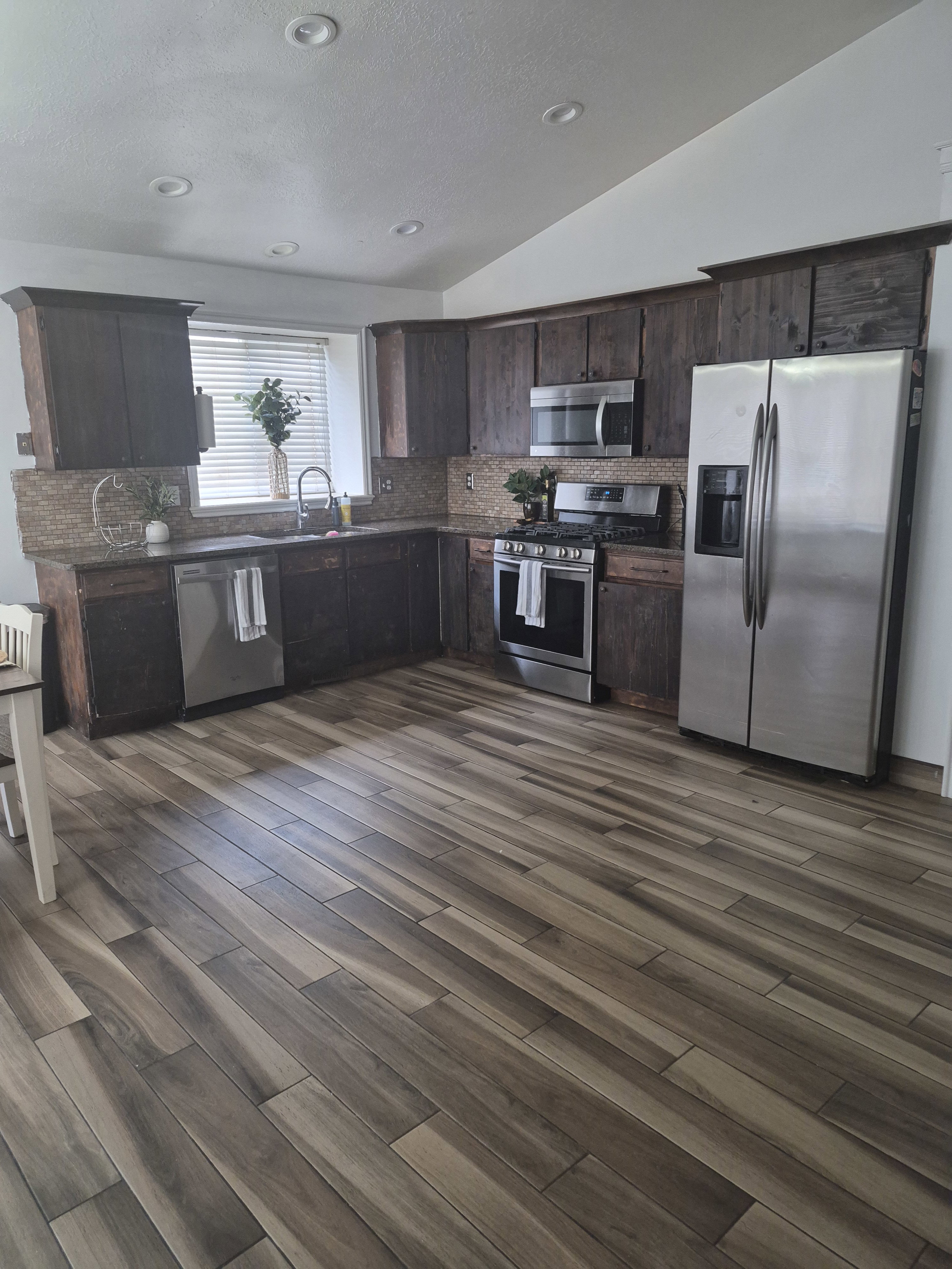 Spacious kitchen featuring dark wood cabinetry, stainless steel appliances, wood-finish flooring, recessed lighting, and a mosaic tile backsplash