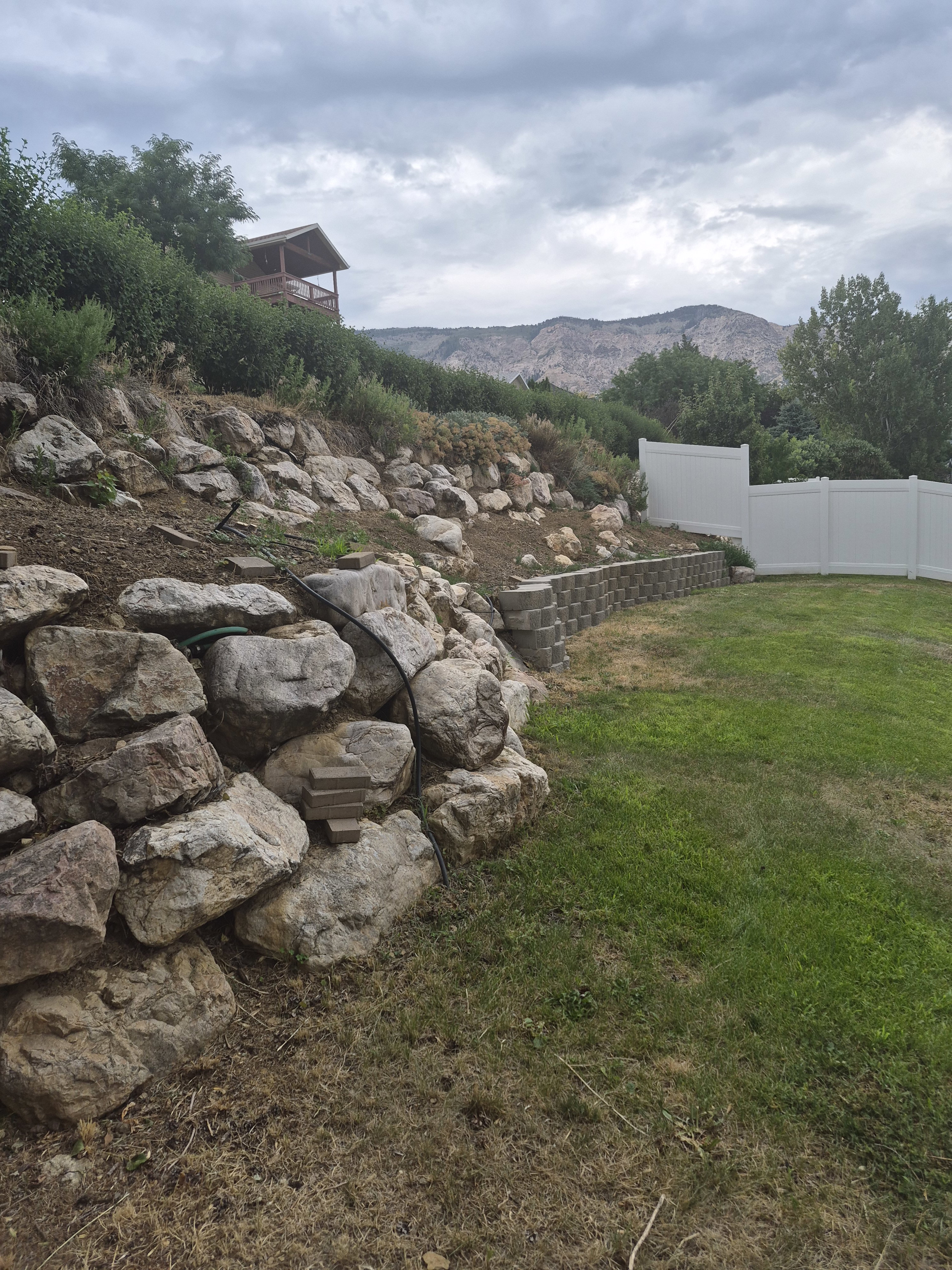 Expansive yard featuring a large rock retaining wall, terraced planting areas, and a block retaining wall
