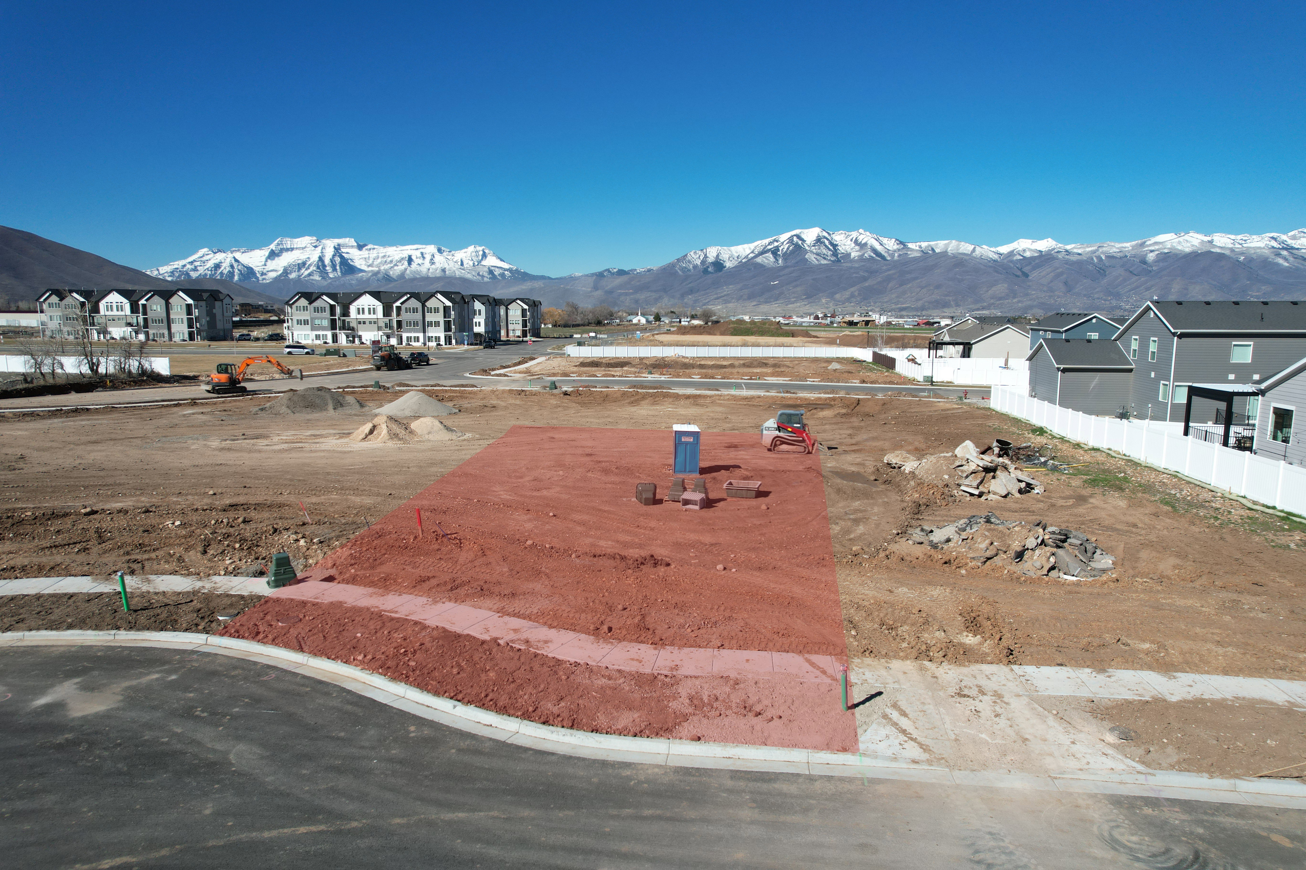 Cleared land parcel featuring visible lot boundaries, a paved street front, and distant mountain backdrops