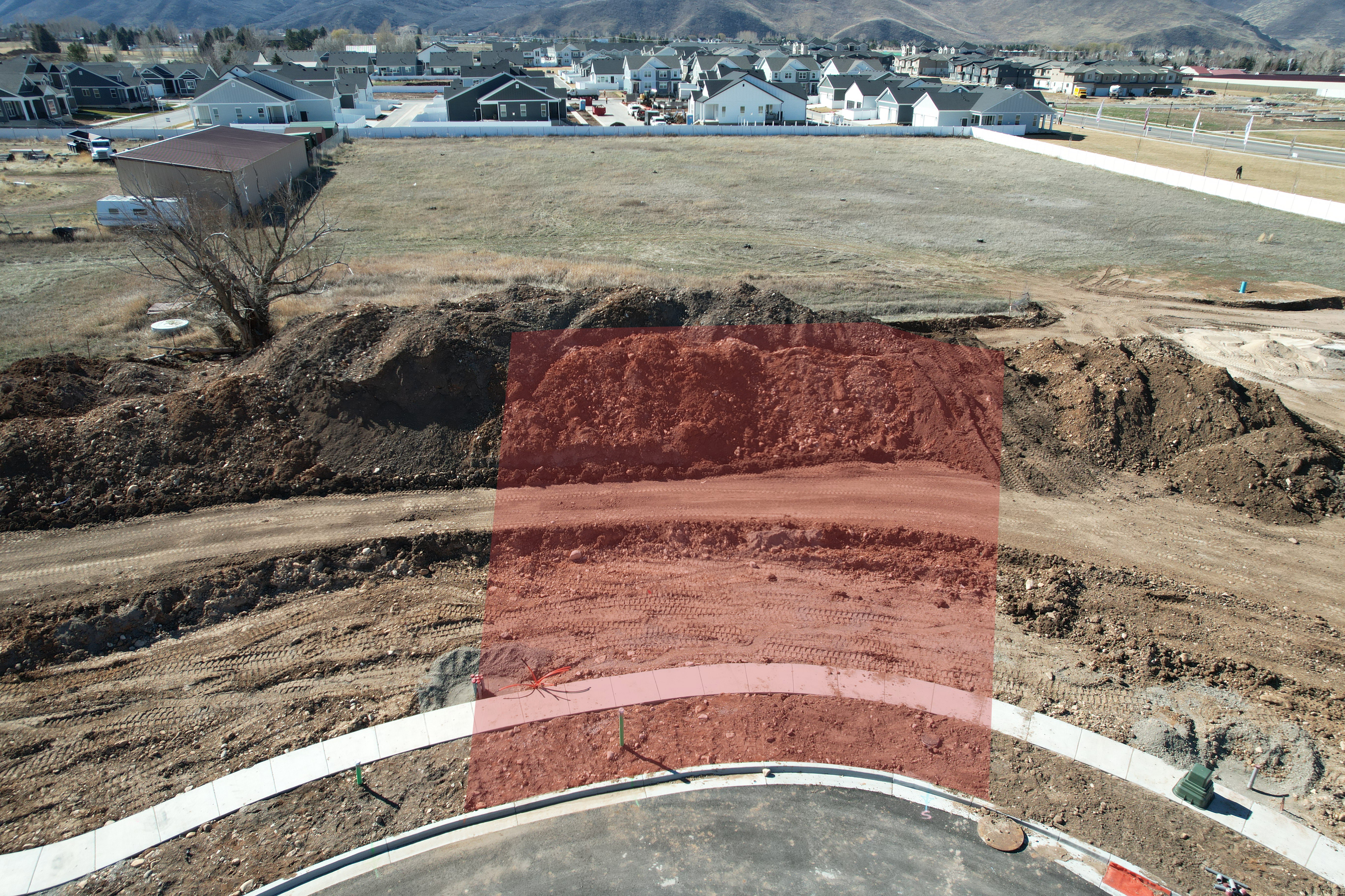 Graded building lot featuring a completed street with sidewalk and curb, surrounded by undeveloped land