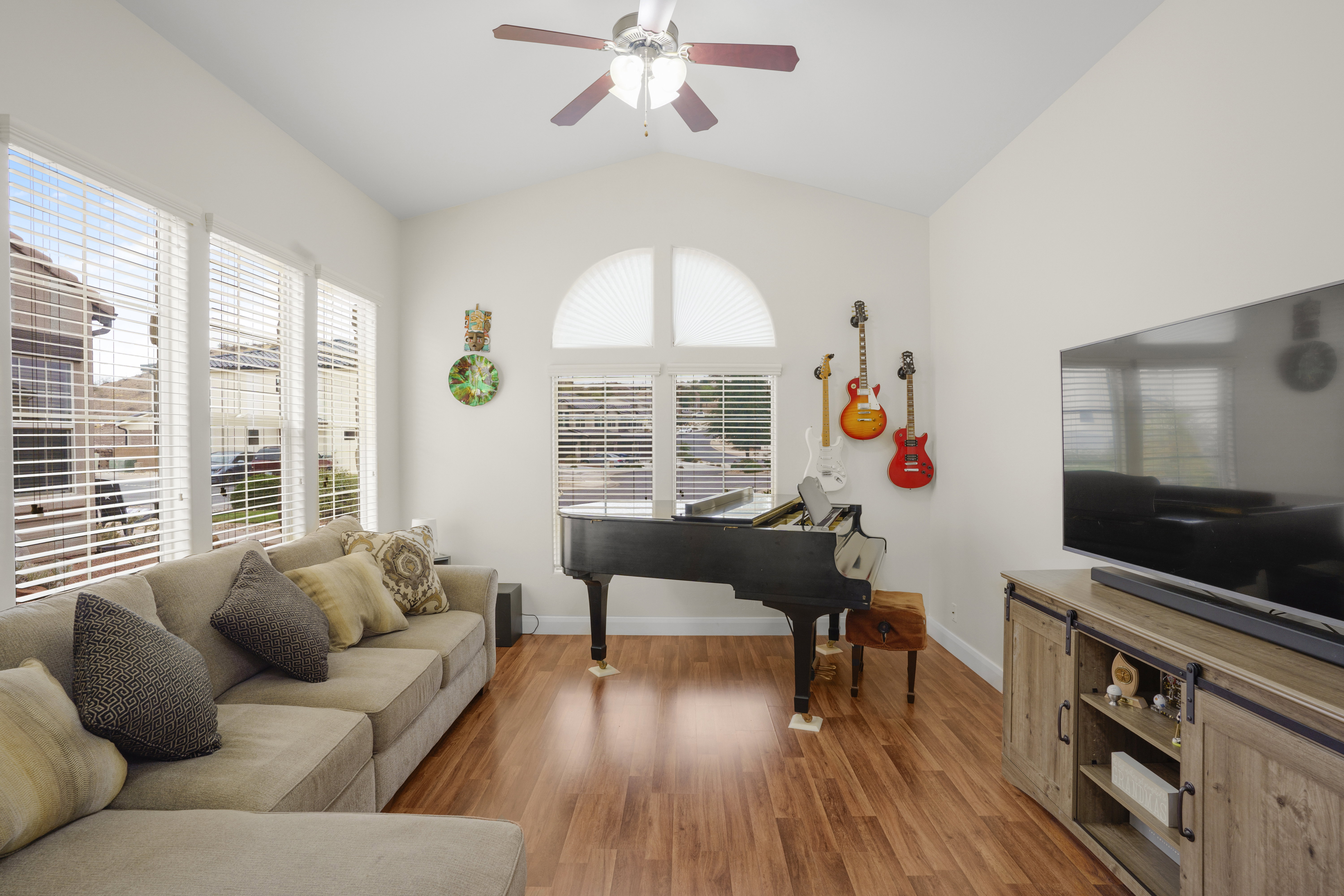 Vaulted ceiling living space with wood-finish flooring, multiple large windows, and a ceiling fan