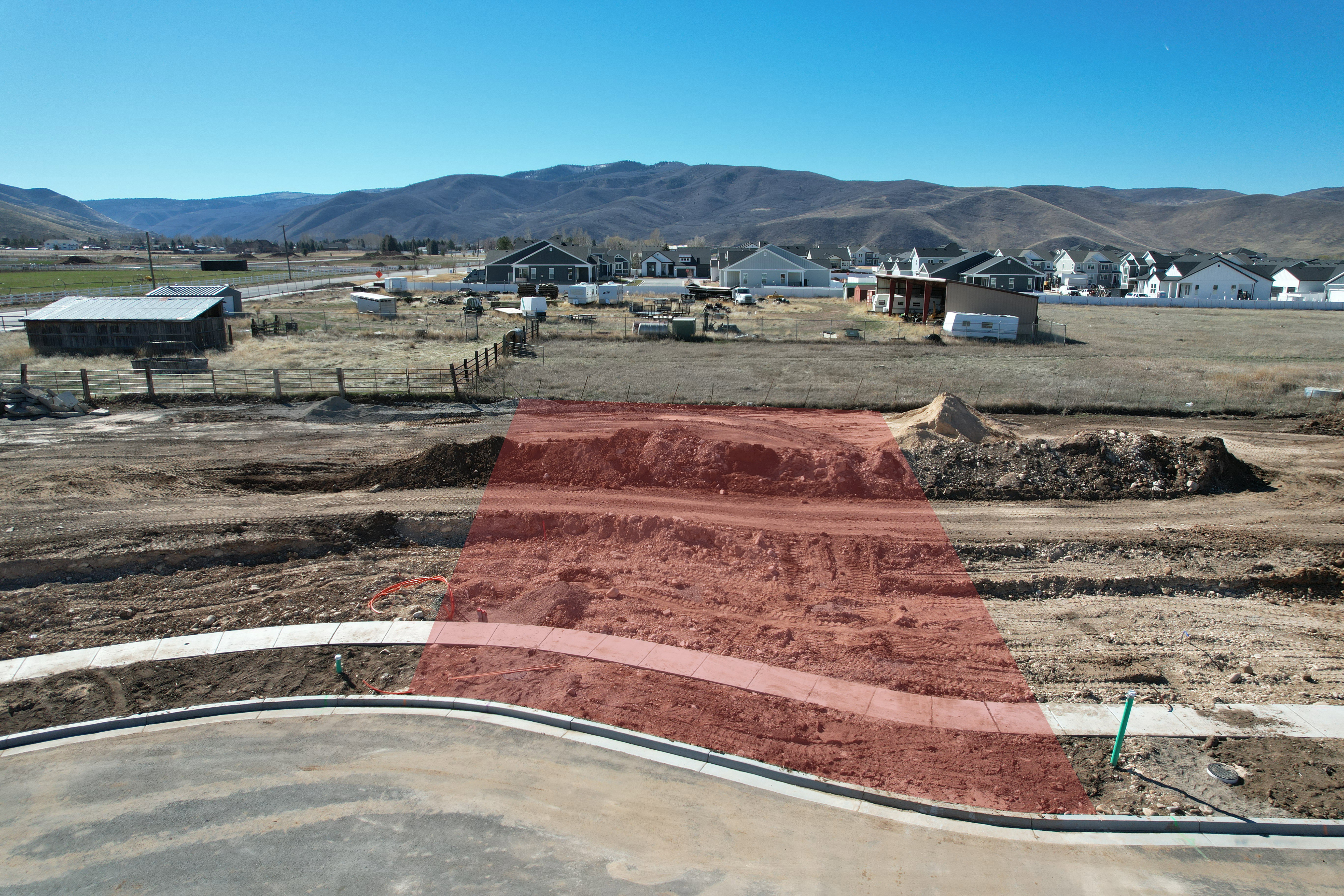 Developable land lot featuring a paved road, concrete sidewalk, and mountain backdrop