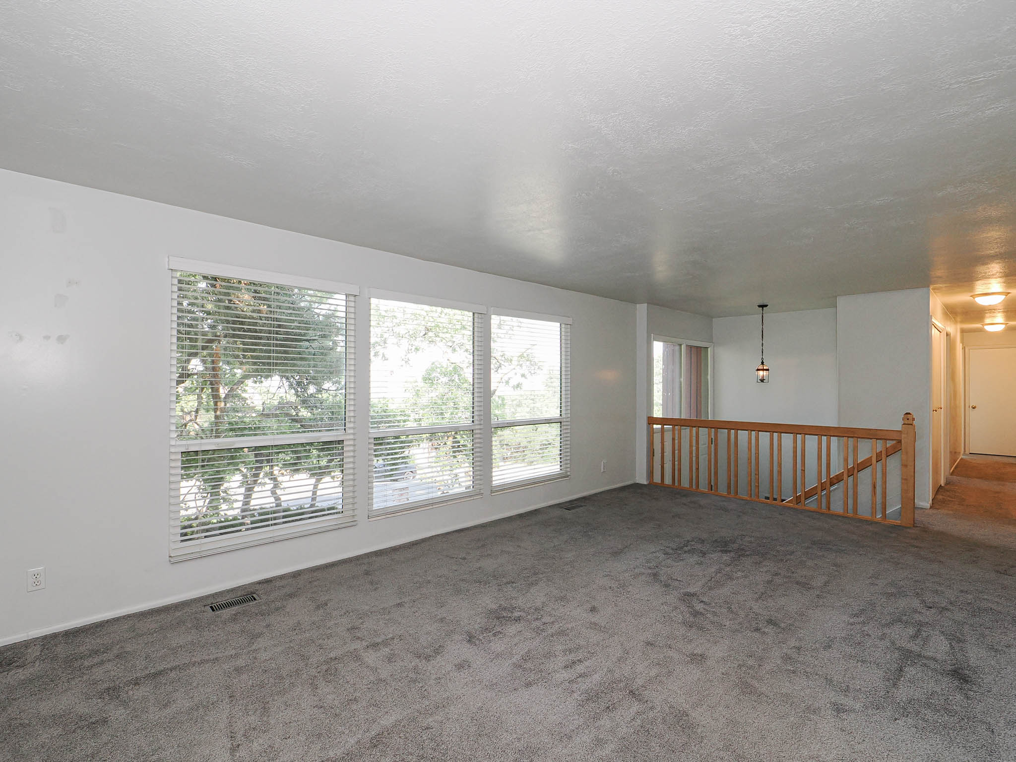 Expansive room with large windows, gray carpeting, white walls, and a light wood railing