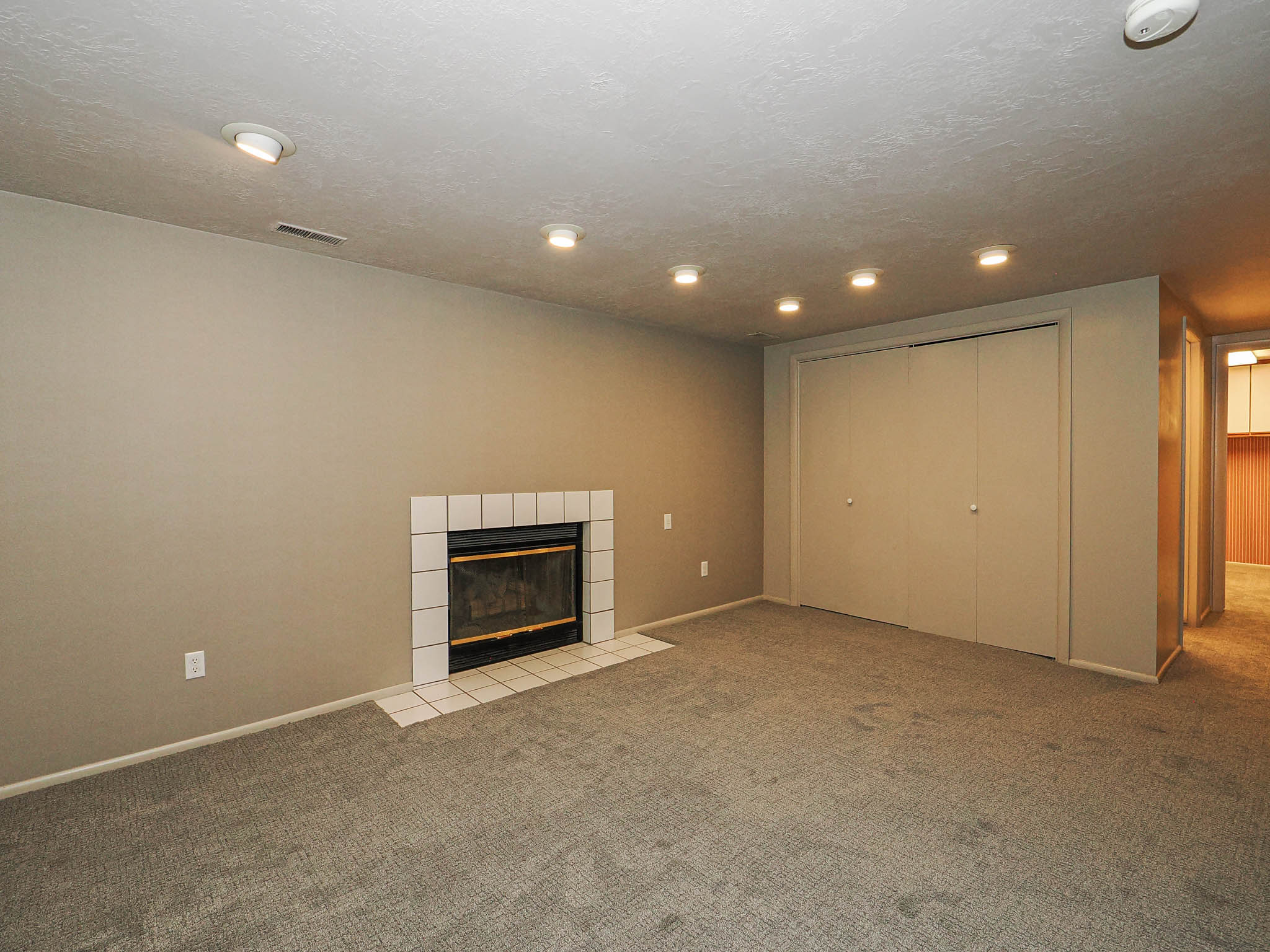 Carpeted room featuring a white-tiled fireplace with a glass enclosure, recessed ceiling lighting, and a bi-fold closet