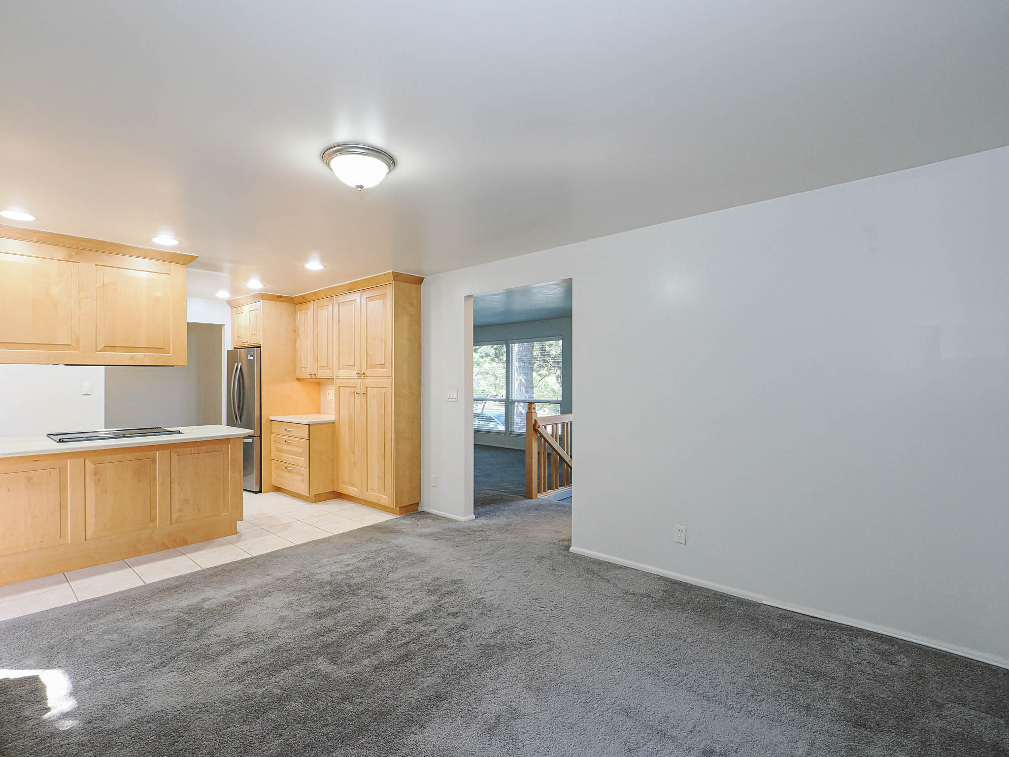 Open-concept living area with light wood-finish cabinetry, stainless steel refrigerator, recessed lighting, and a kitchen island featuring a smooth cooktop