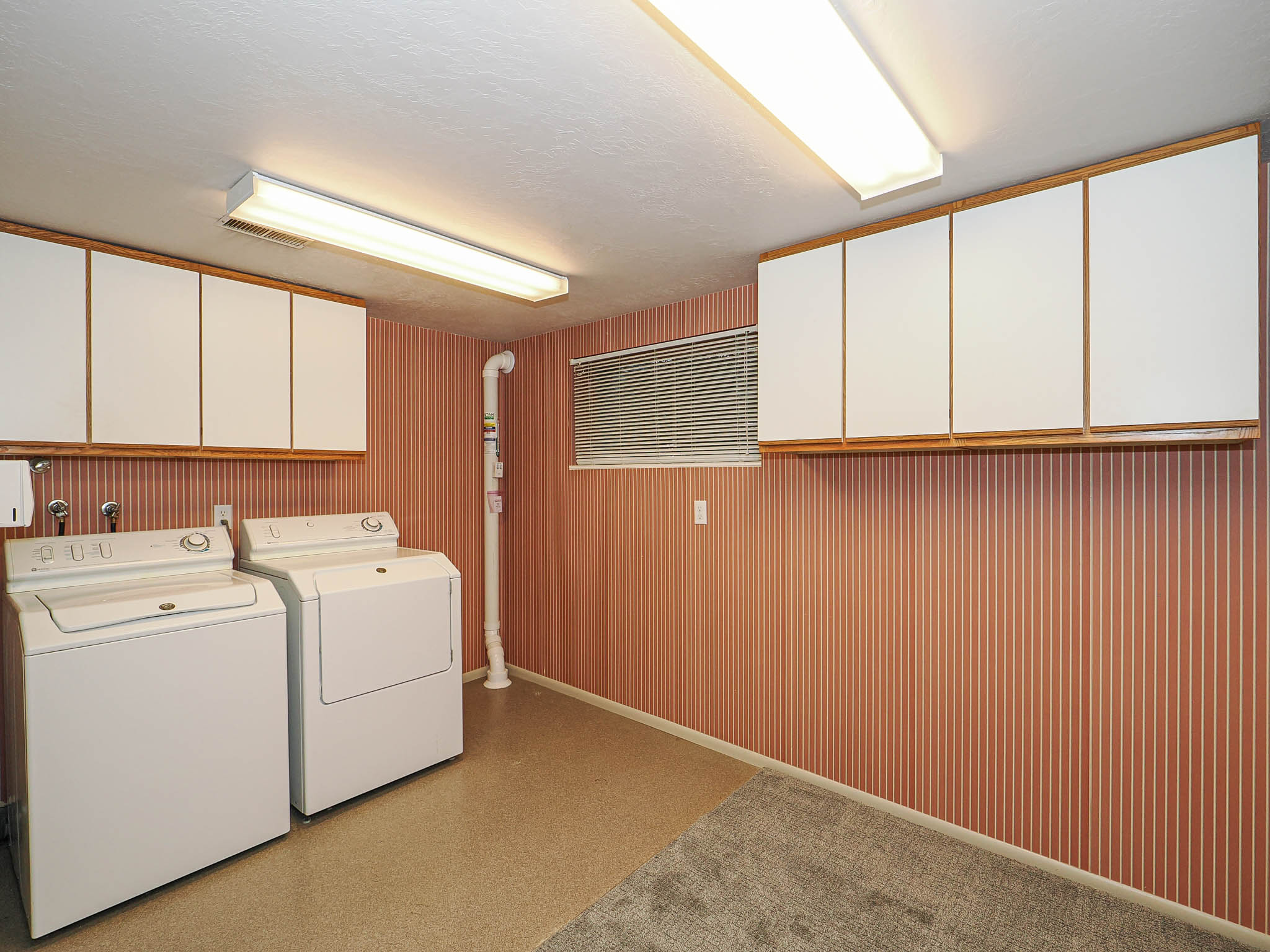 Dedicated laundry area featuring overhead cabinetry, wall-mounted shelving, and a small window with blinds