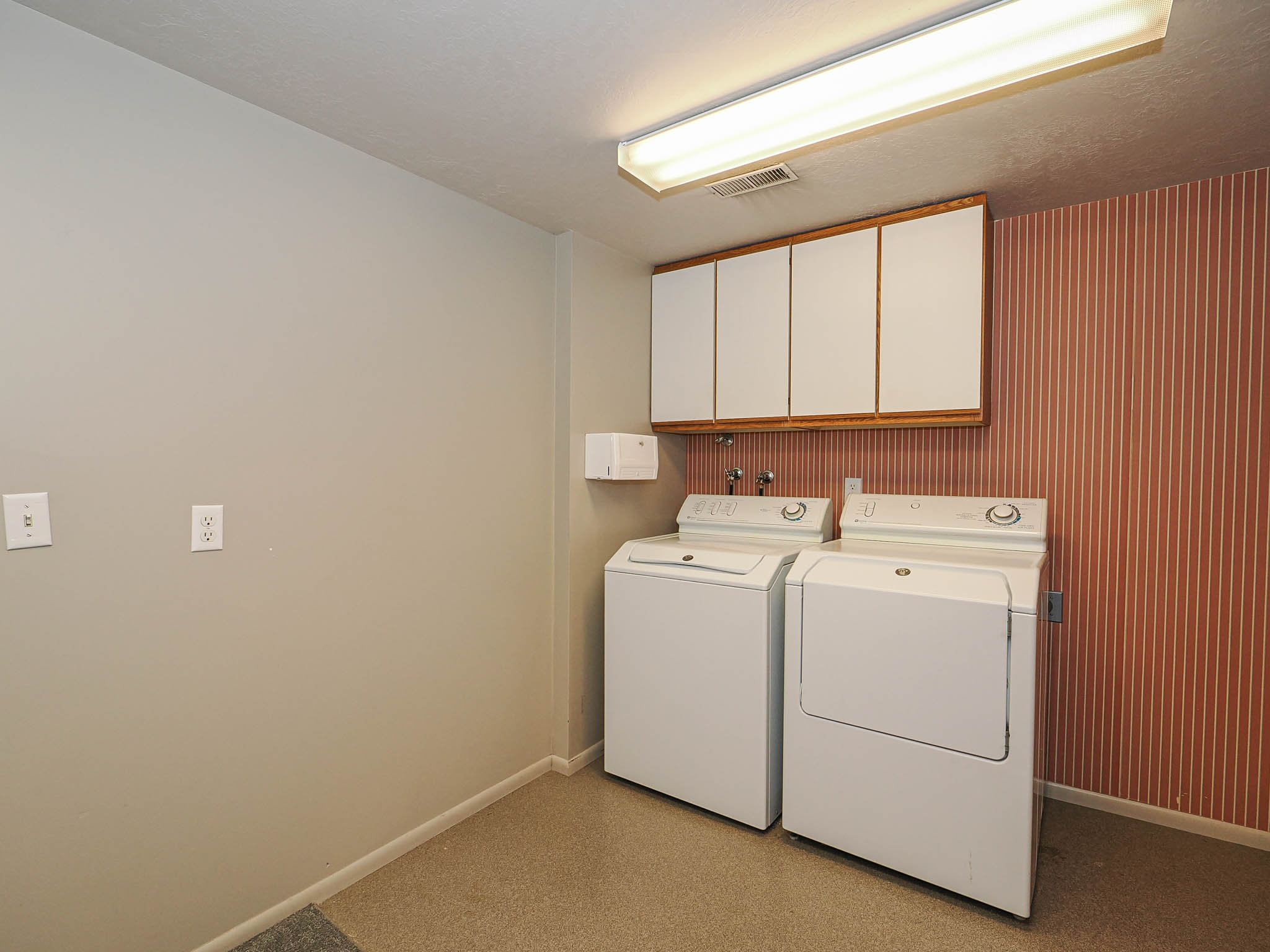 Dedicated laundry area featuring overhead cabinetry with wood-finish trim, a utility sink hookup, and durable flooring