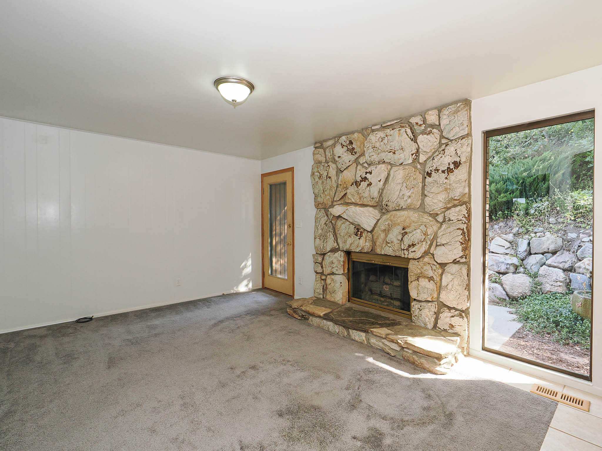 Stone fireplace with hearth, full-height window, paneled wall, wood-frame door, and ceiling-mounted light fixture
