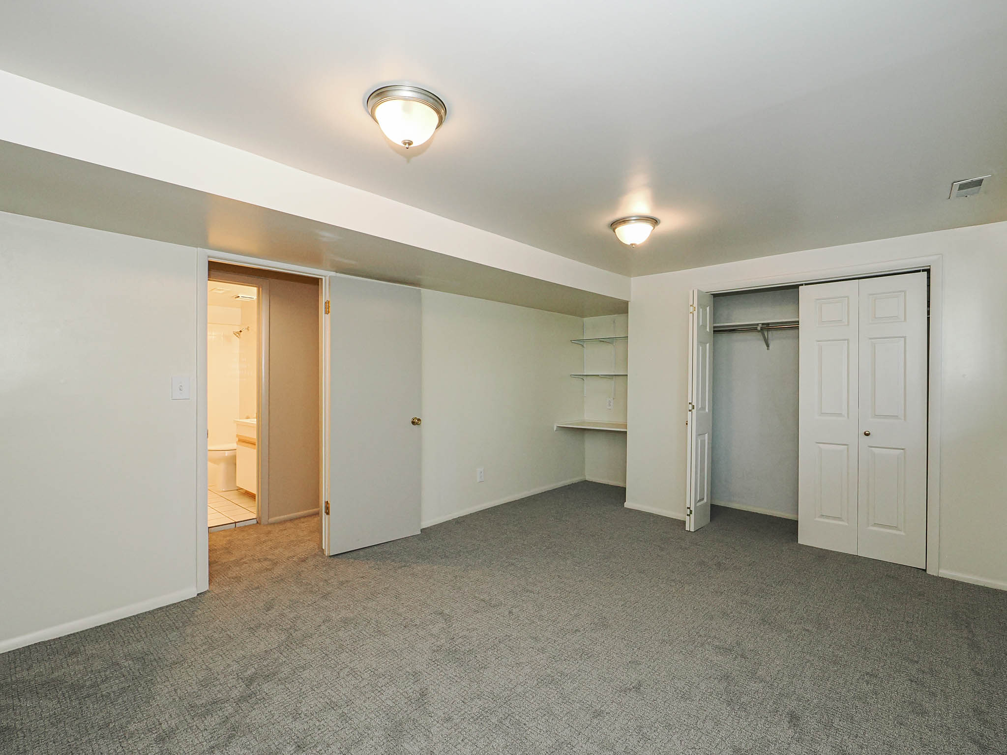 Spacious room featuring neutral carpeting, a built-in shelving unit with desk space, and a double-door closet