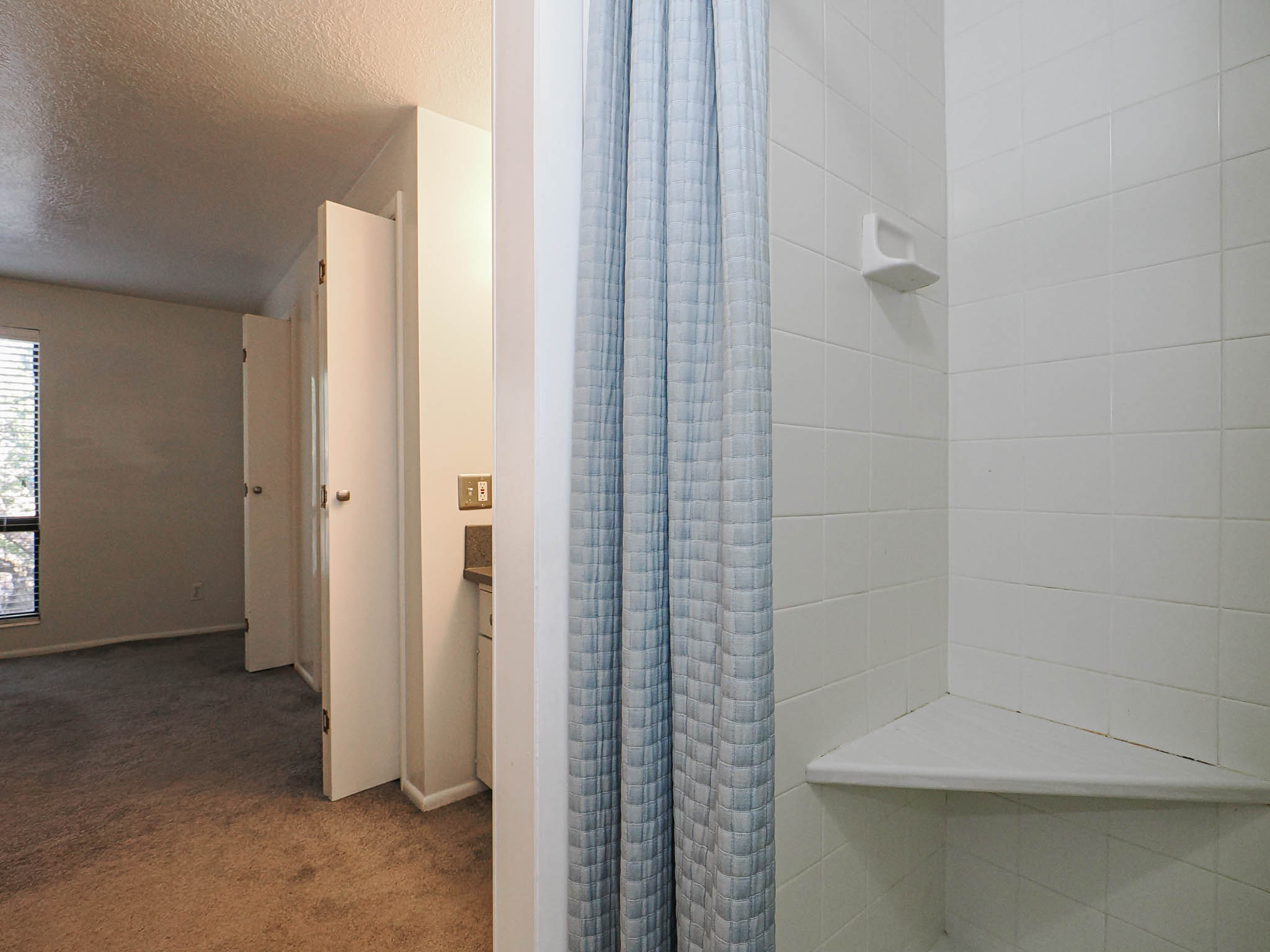 Shower enclosure featuring white ceramic tile walls and a built-in corner shelf