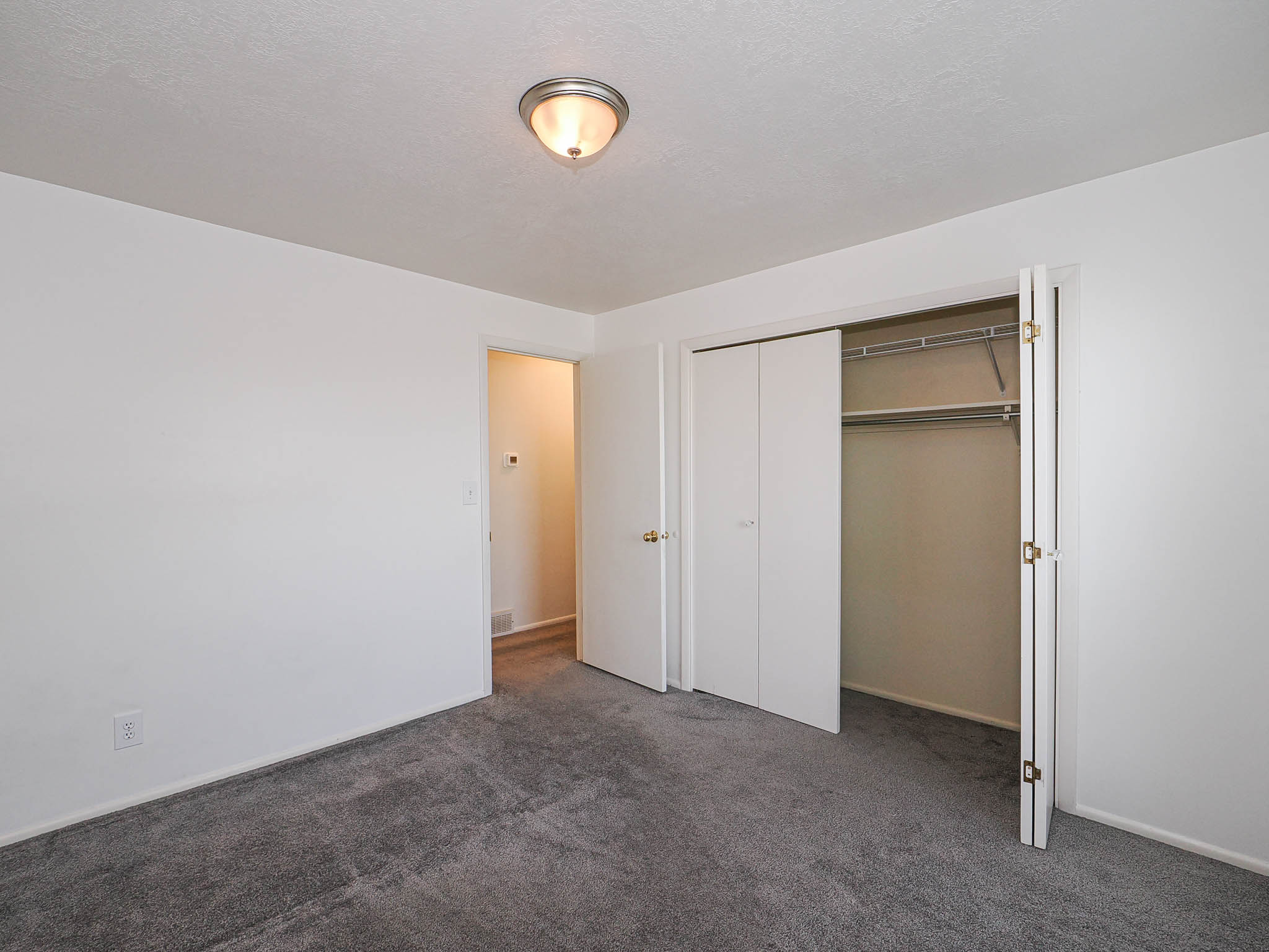 Carpeted room featuring white walls, a flush-mount ceiling light, and a bi-fold closet with shelving and a hanging rod