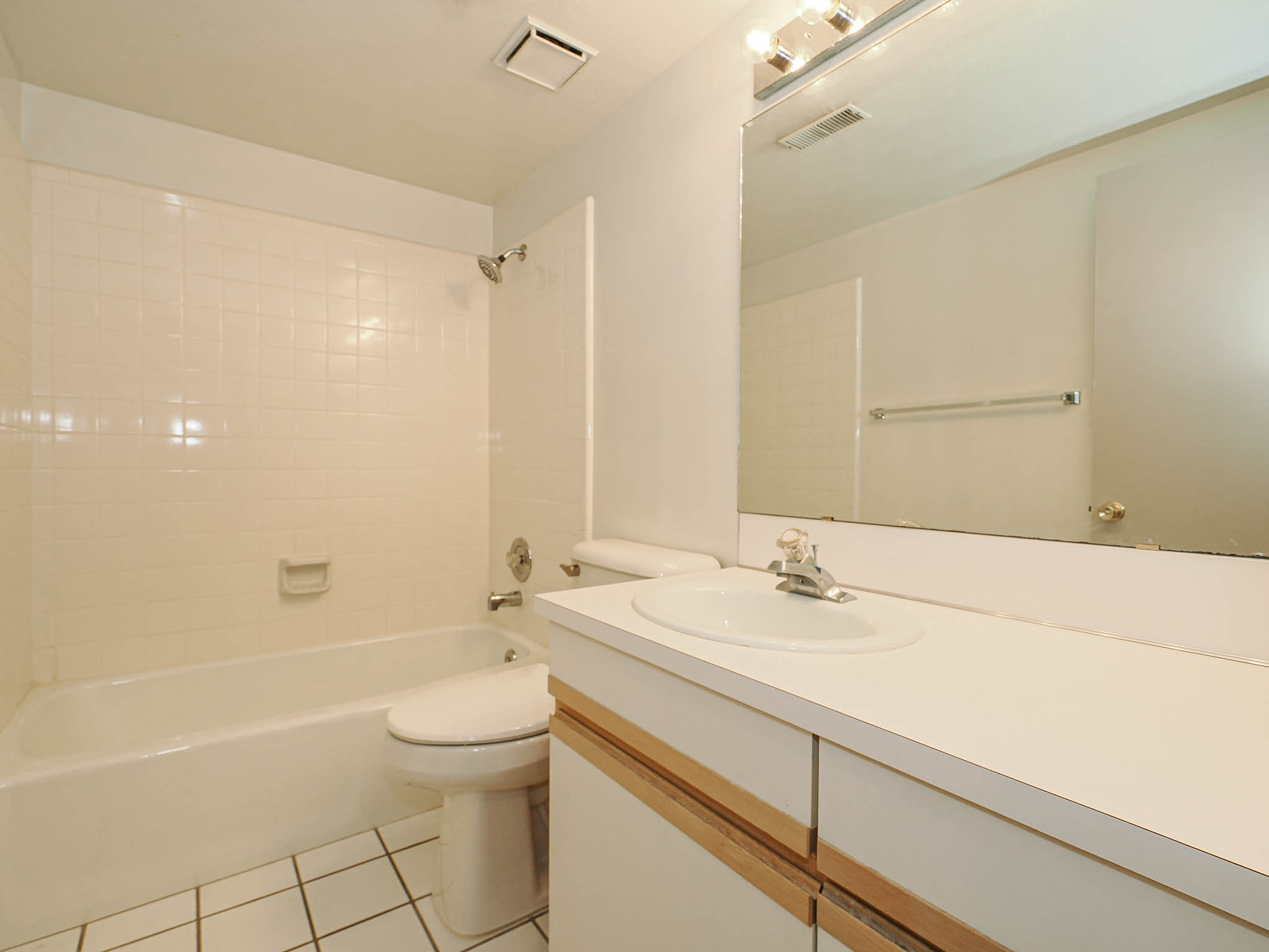 Full bathroom featuring a white tile shower surround, integrated bathtub, and a single vanity with a laminate countertop and base cabinetry