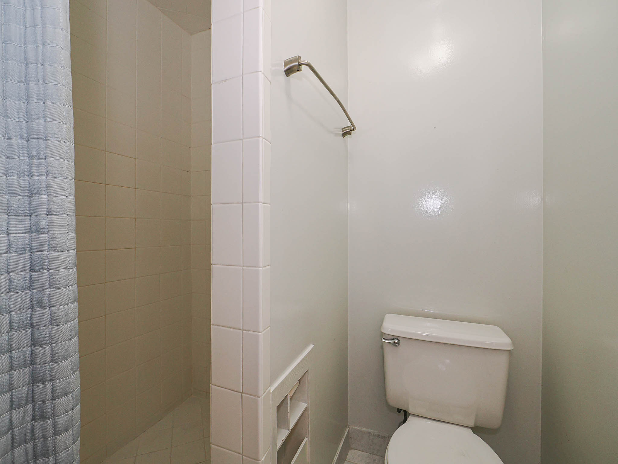Bathroom featuring a tiled shower enclosure, white walls, a standard toilet, and a towel bar