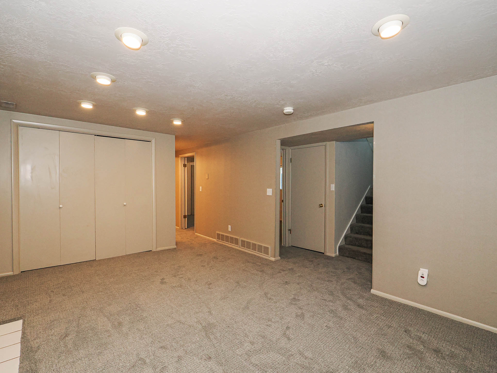 Carpeted living area featuring recessed lighting, bi-fold closet doors, a doorway, and a carpeted staircase