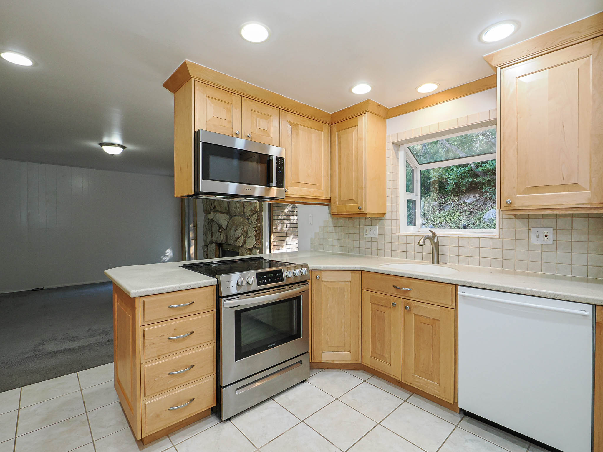 Kitchen featuring wood cabinetry, stainless steel range and microwave, light-toned countertops, and a tile backsplash